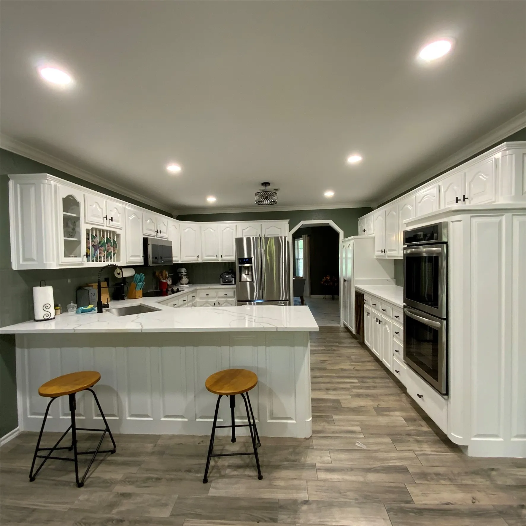 White cabinetry with dark hardware, stainless steel appliances, light-toned countertops, wood-finish flooring, and recessed lighting