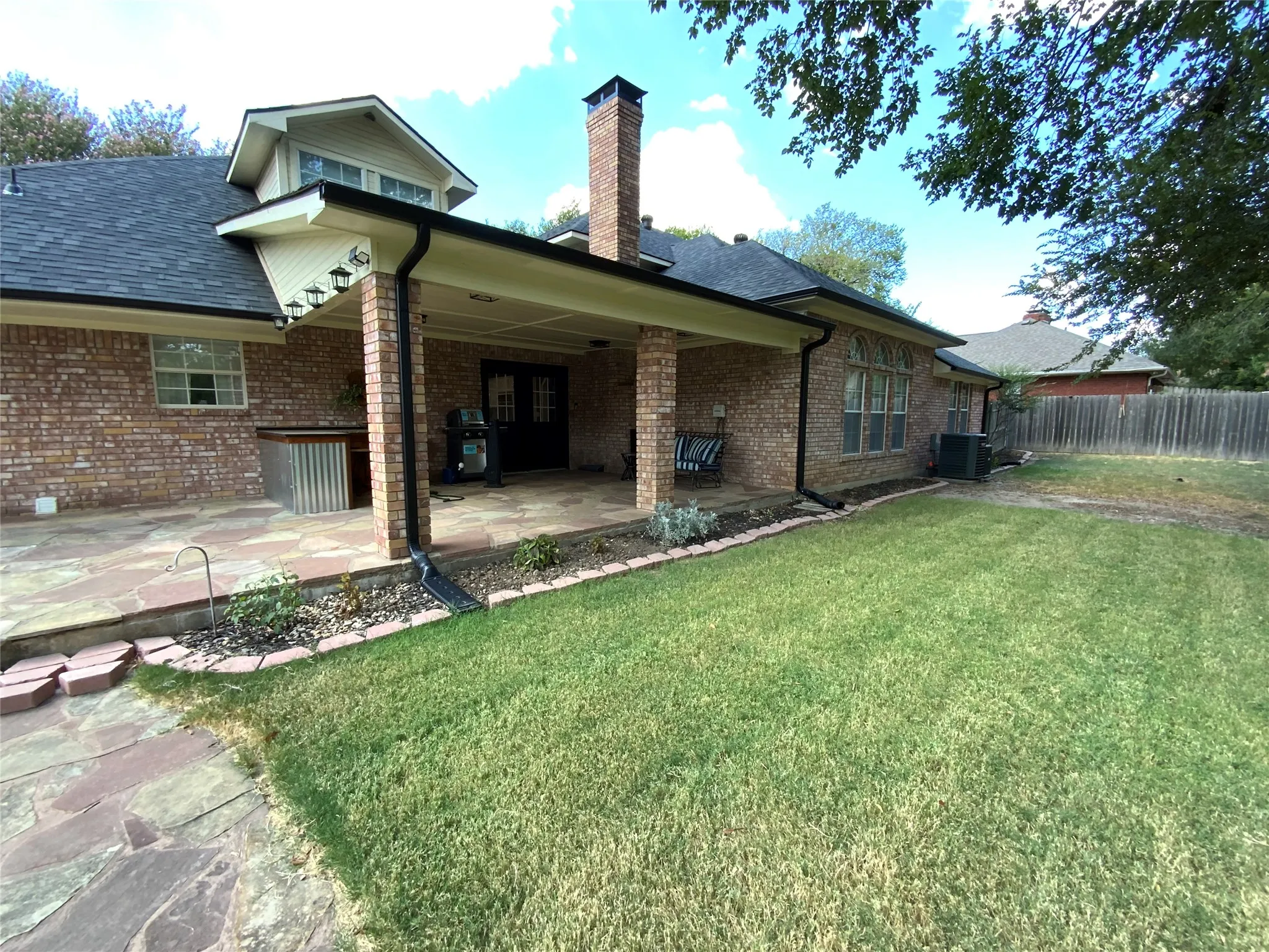 Expansive backyard featuring a covered patio with flagstone flooring, brick pillars, a built-in outdoor bar, and double French doors