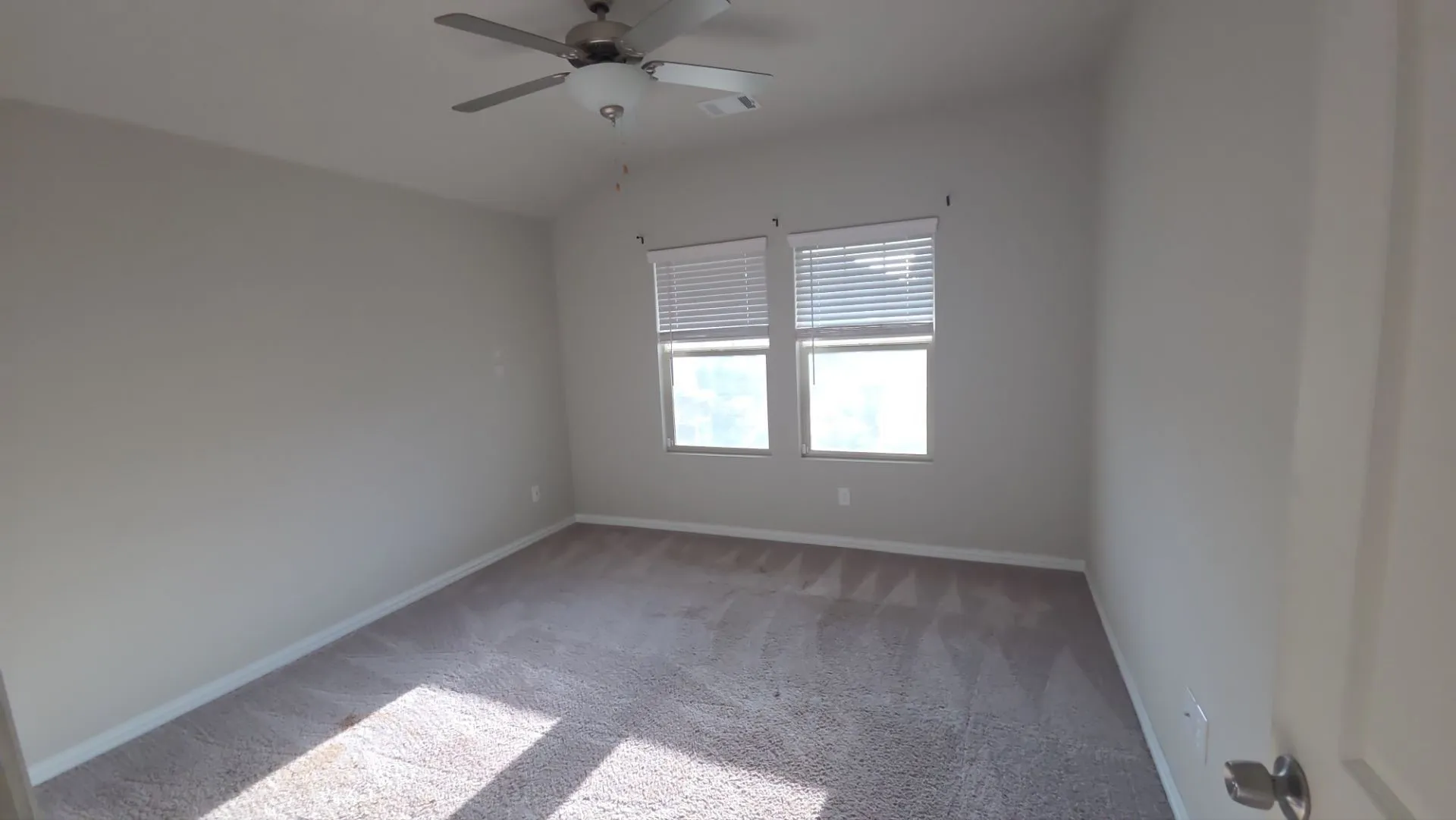 Neutral-toned carpeting, two windows with blinds, a ceiling fan with integrated lighting, and light-colored wall finishes