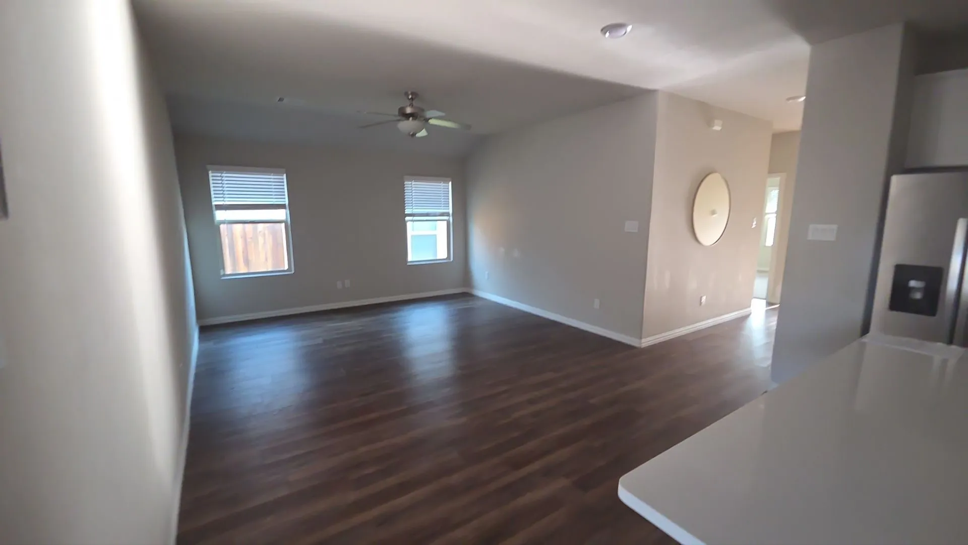 Spacious living area featuring wood-finish flooring, two windows with blinds, a ceiling fan, and recessed lighting