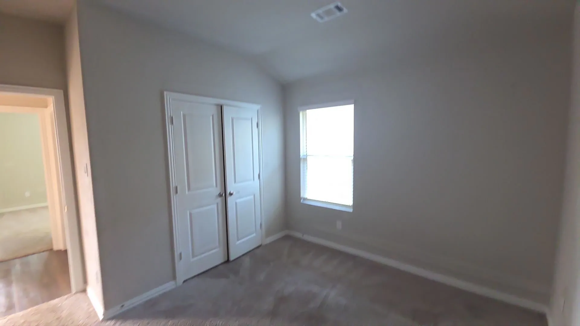 Vaulted ceiling, neutral tone walls, window with blinds, carpet flooring, and bi-fold closet doors