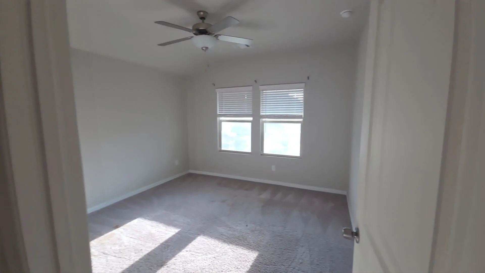 Carpeted room featuring a ceiling fan, two windows with blinds, and neutral wall paint