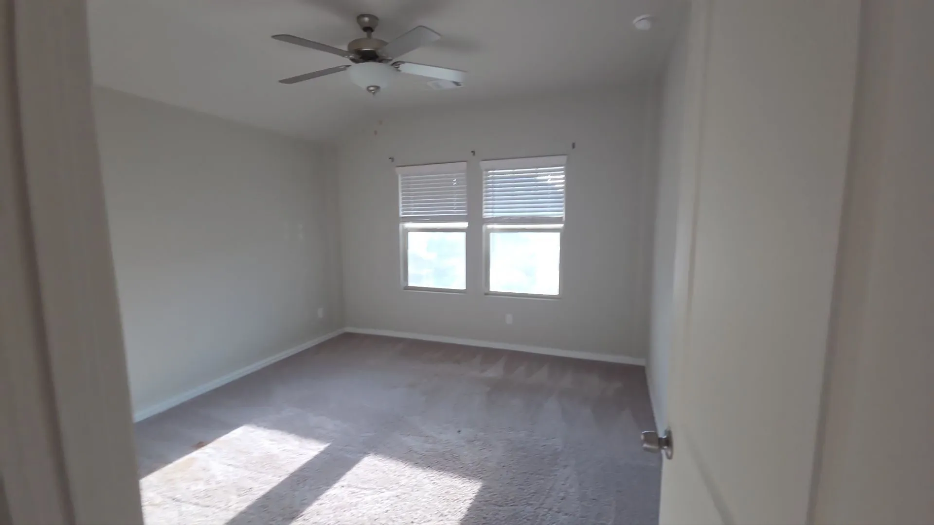 Carpeted room with a ceiling fan, two windows, and horizontal blinds