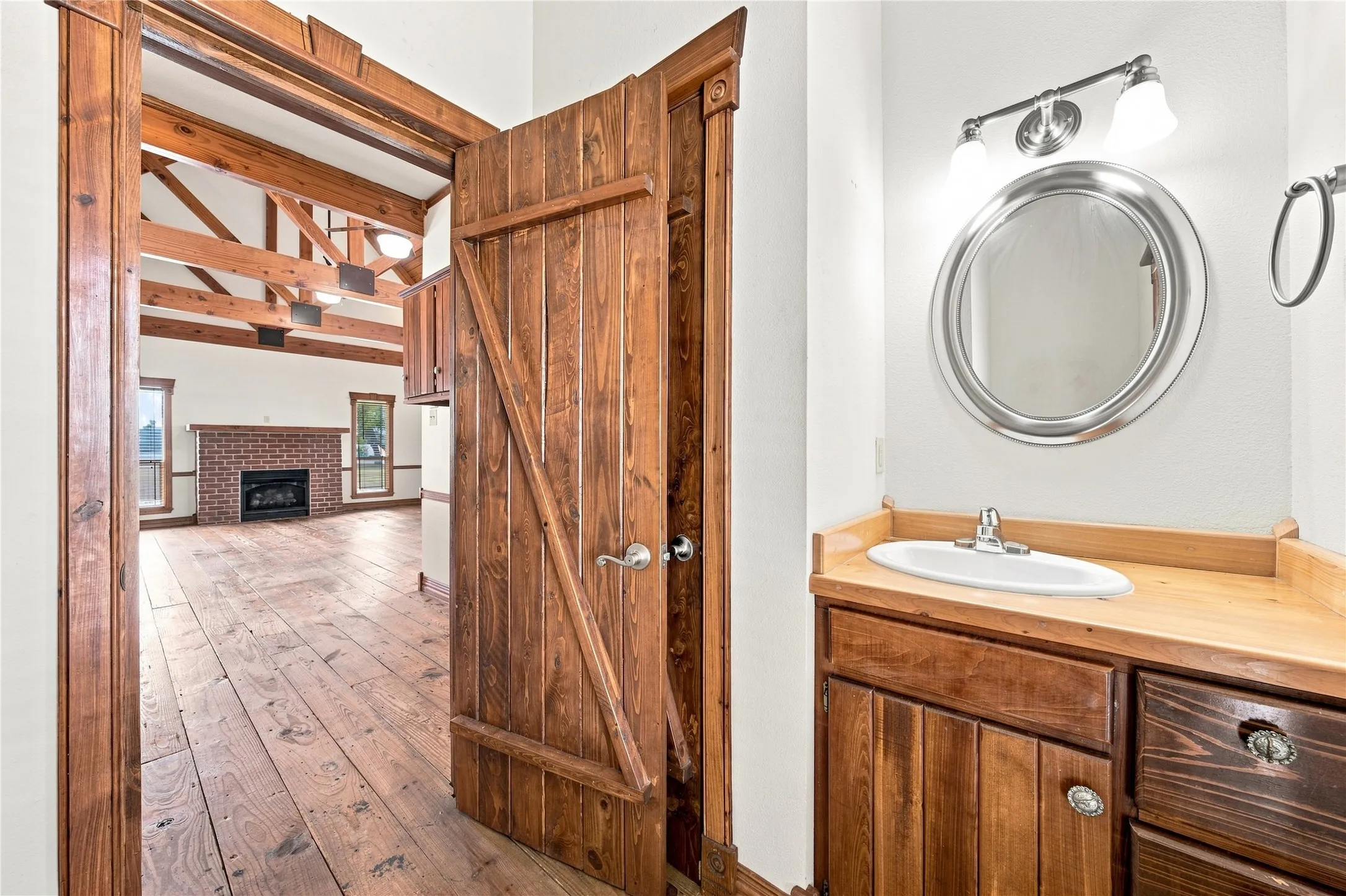 Exposed wood beam ceiling, brick fireplace, wood-finish flooring, and a vanity with wood-finish cabinetry