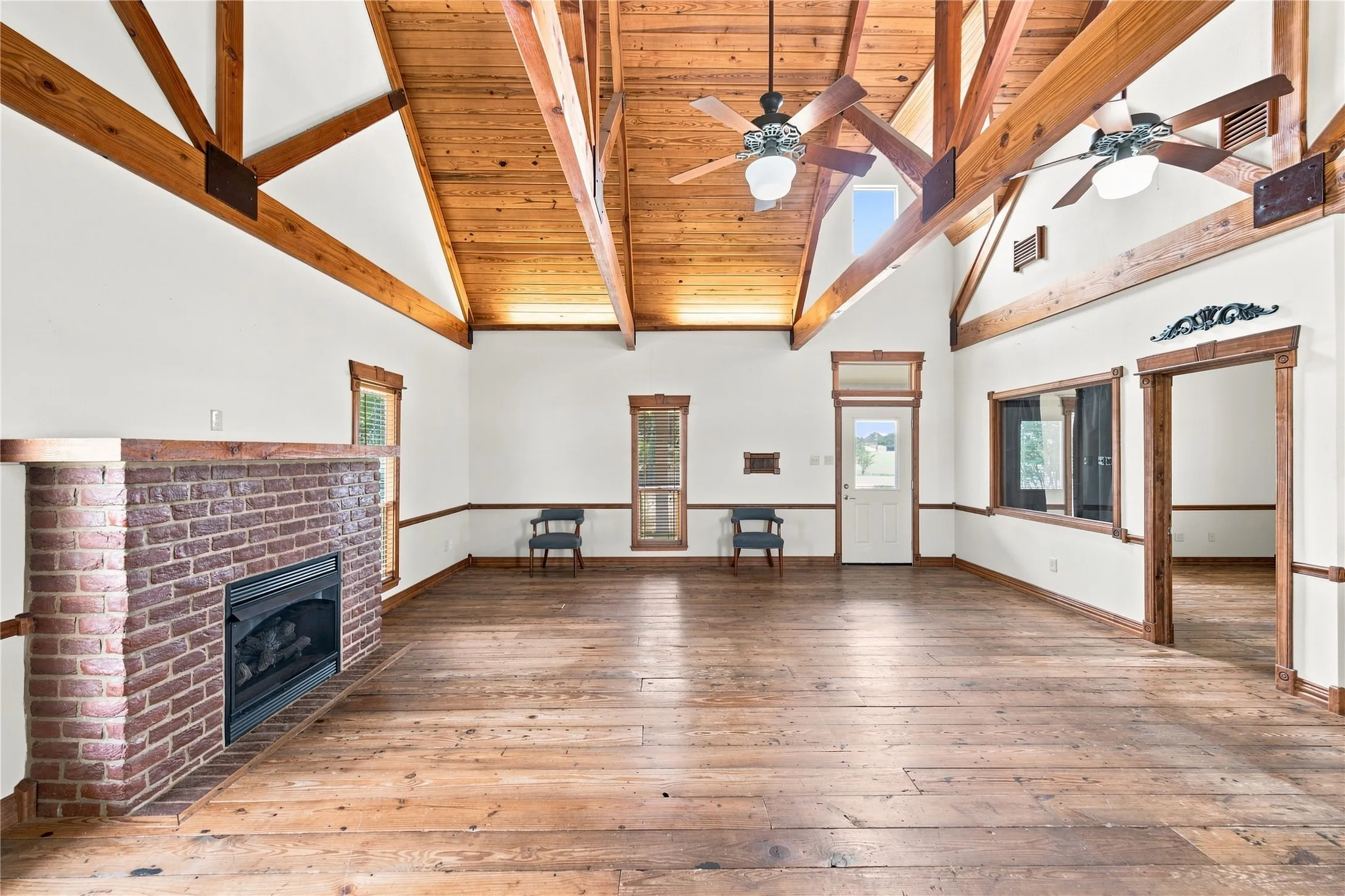 Vaulted wood-paneled ceilings with exposed wood beams, brick fireplace, wood-finish flooring, and multiple windows
