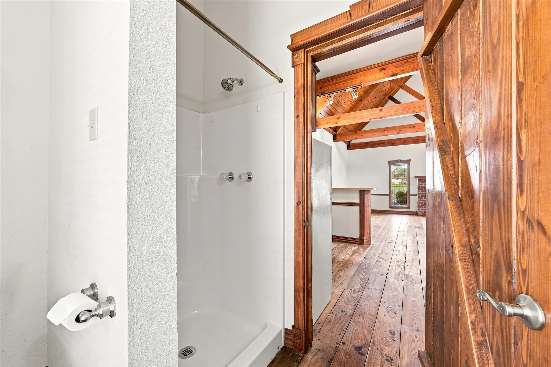 Wood-paneled barn door entry to a room featuring exposed wood ceiling beams, wood-finish flooring, and a window with exterior views