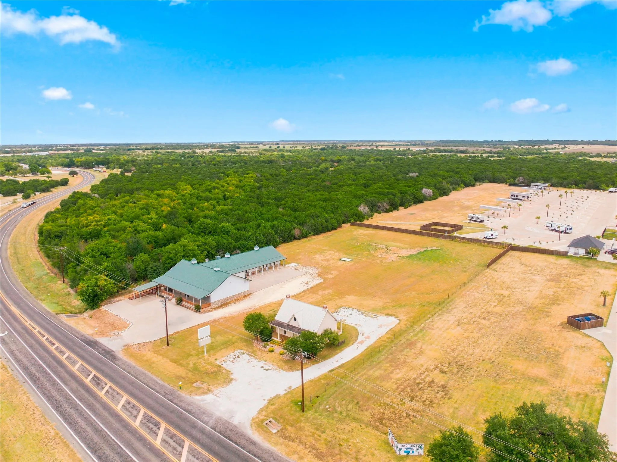 Expansive property featuring a commercial building with a green roof, a separate residential structure, a paved lot with designated spaces, and established trees