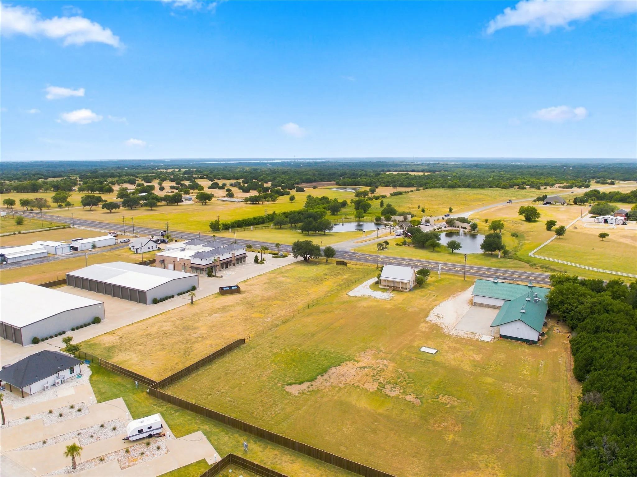 Expansive land parcel with surrounding commercial structures, a paved road, and distant tree lines