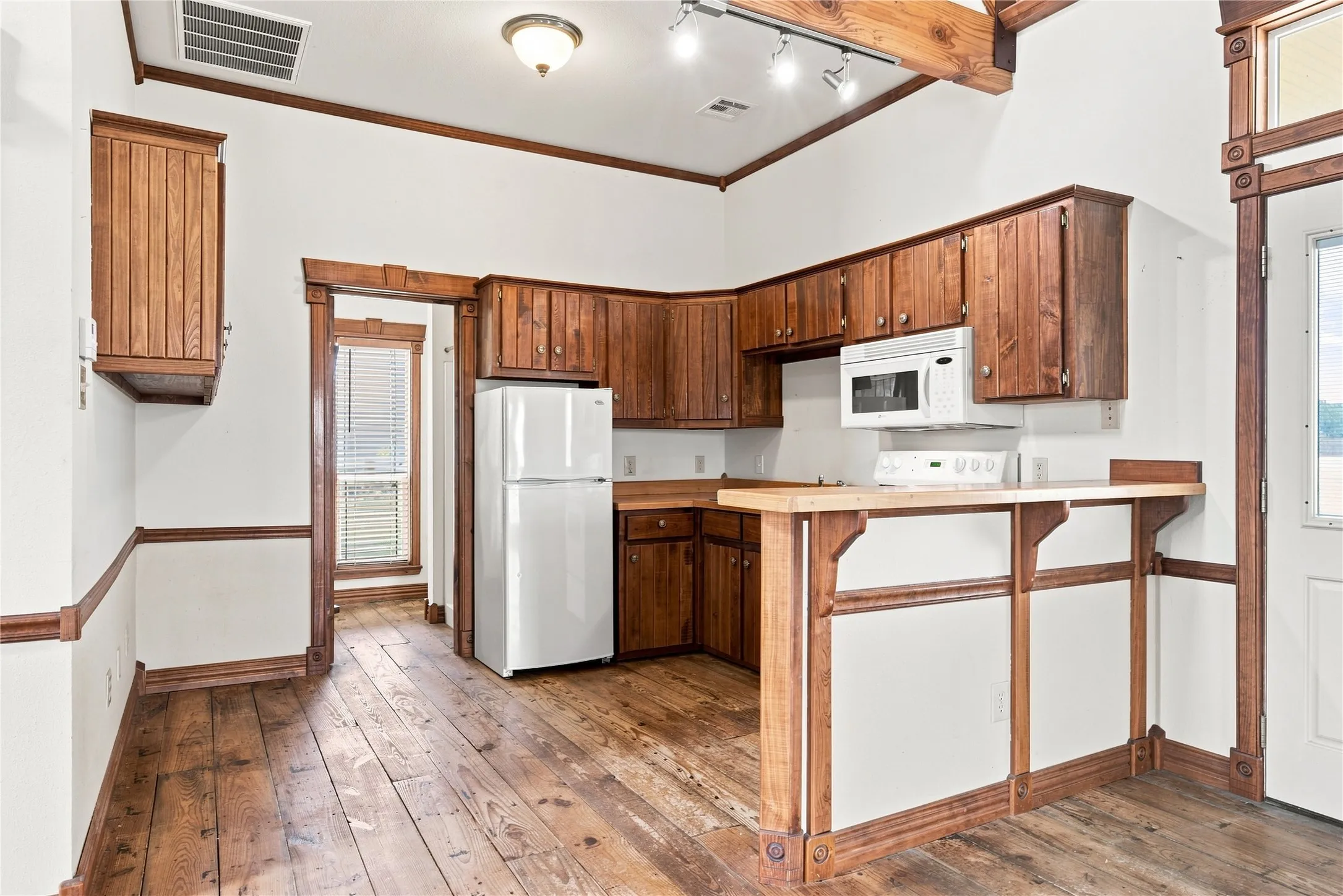 Wood-finish flooring, wood cabinetry, built-in microwave, and exposed wood beams