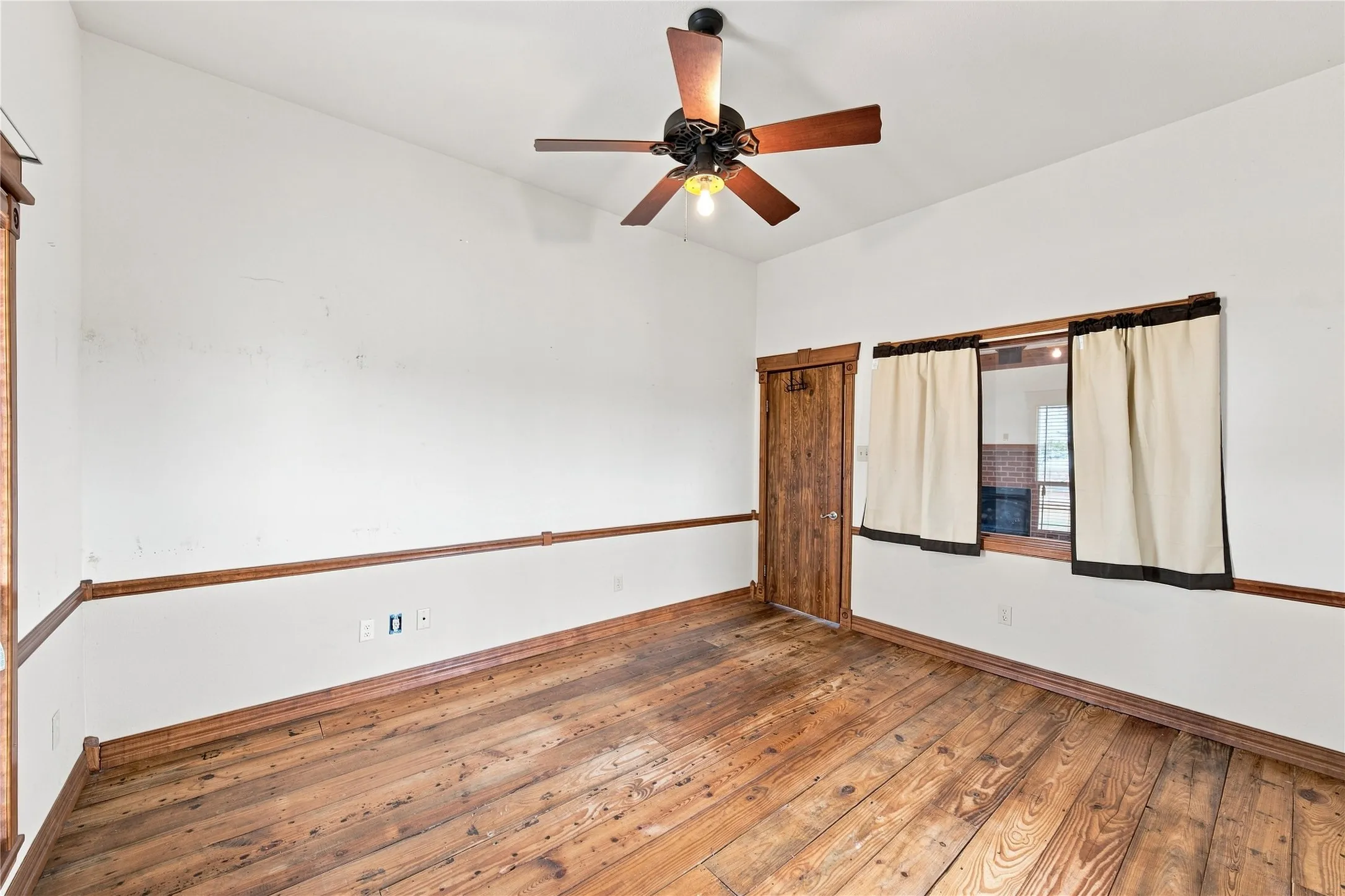 Vaulted ceiling with a ceiling fan, wood-finish flooring, wood trim, and a wood-finish door