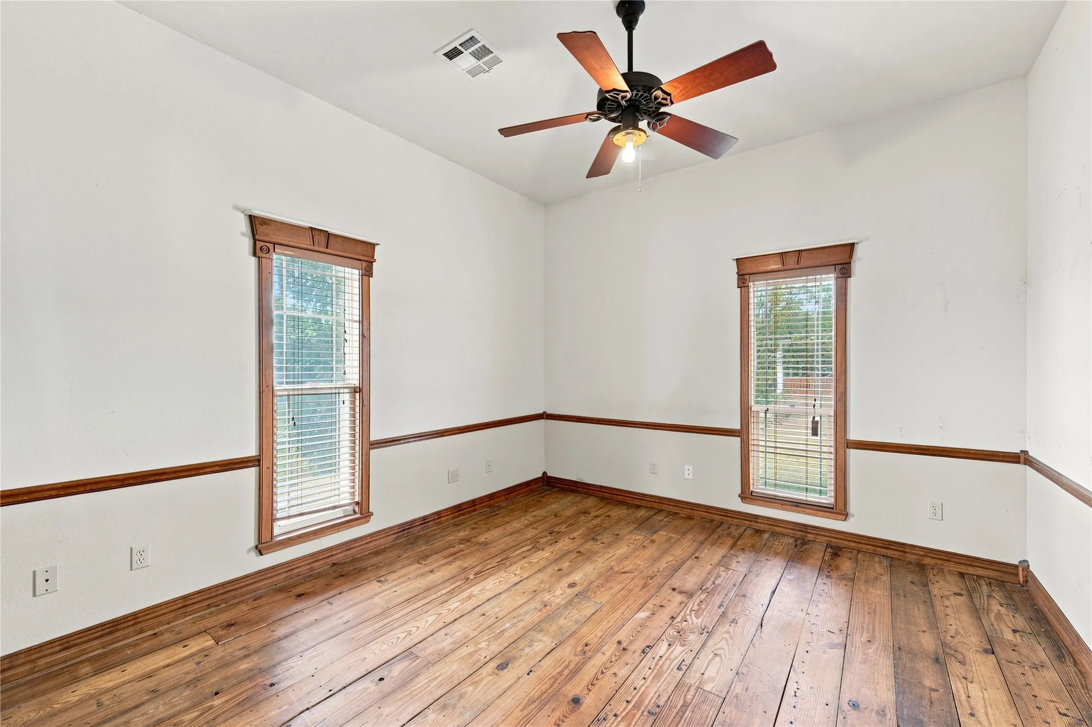Natural wood flooring, wood-trimmed windows, classic chair rail molding, and a ceiling fan with light fixture