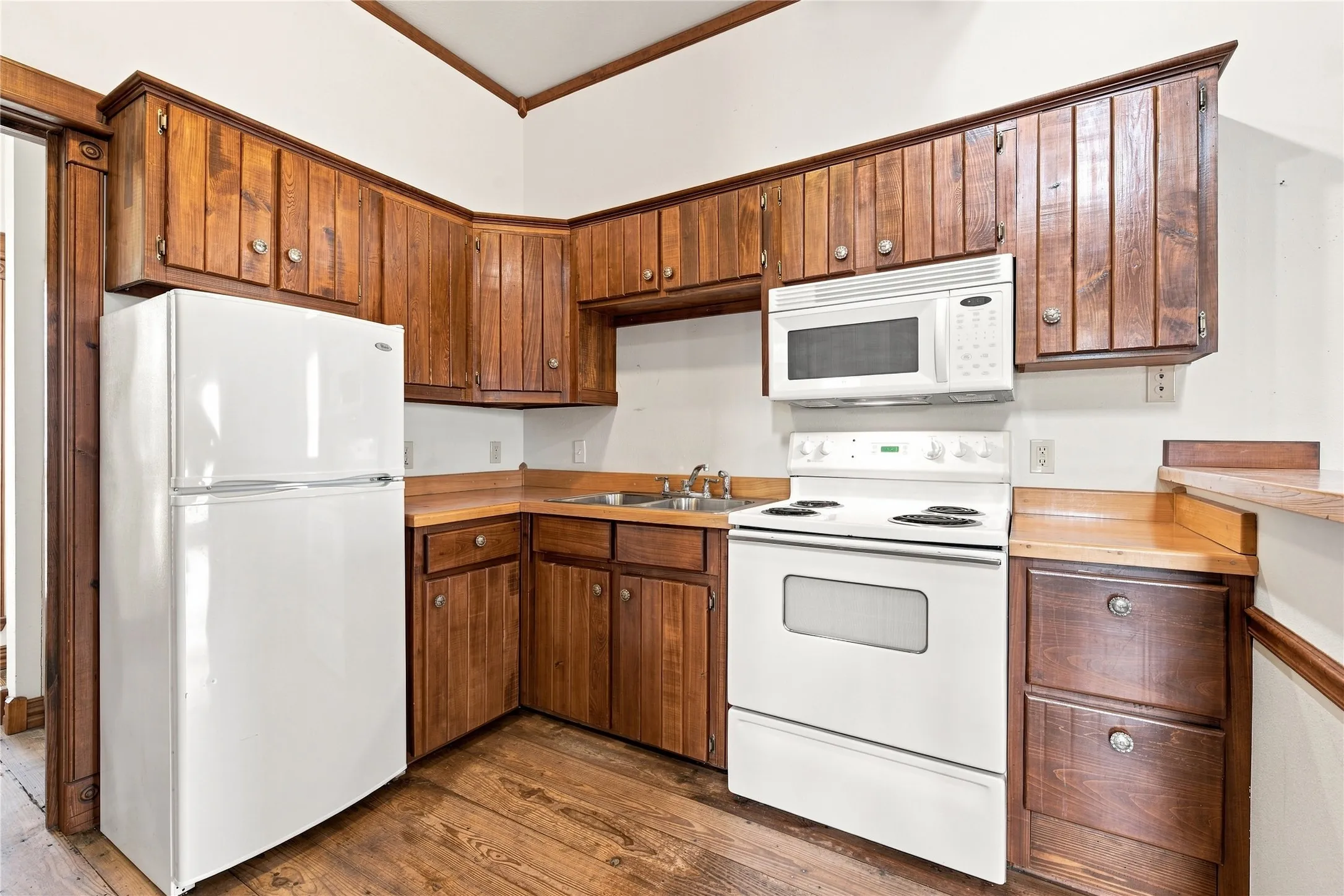 Kitchen featuring wood-finish cabinetry, solid surface countertops, a white top-freezer refrigerator, a white electric range, and an over-the-range microwave