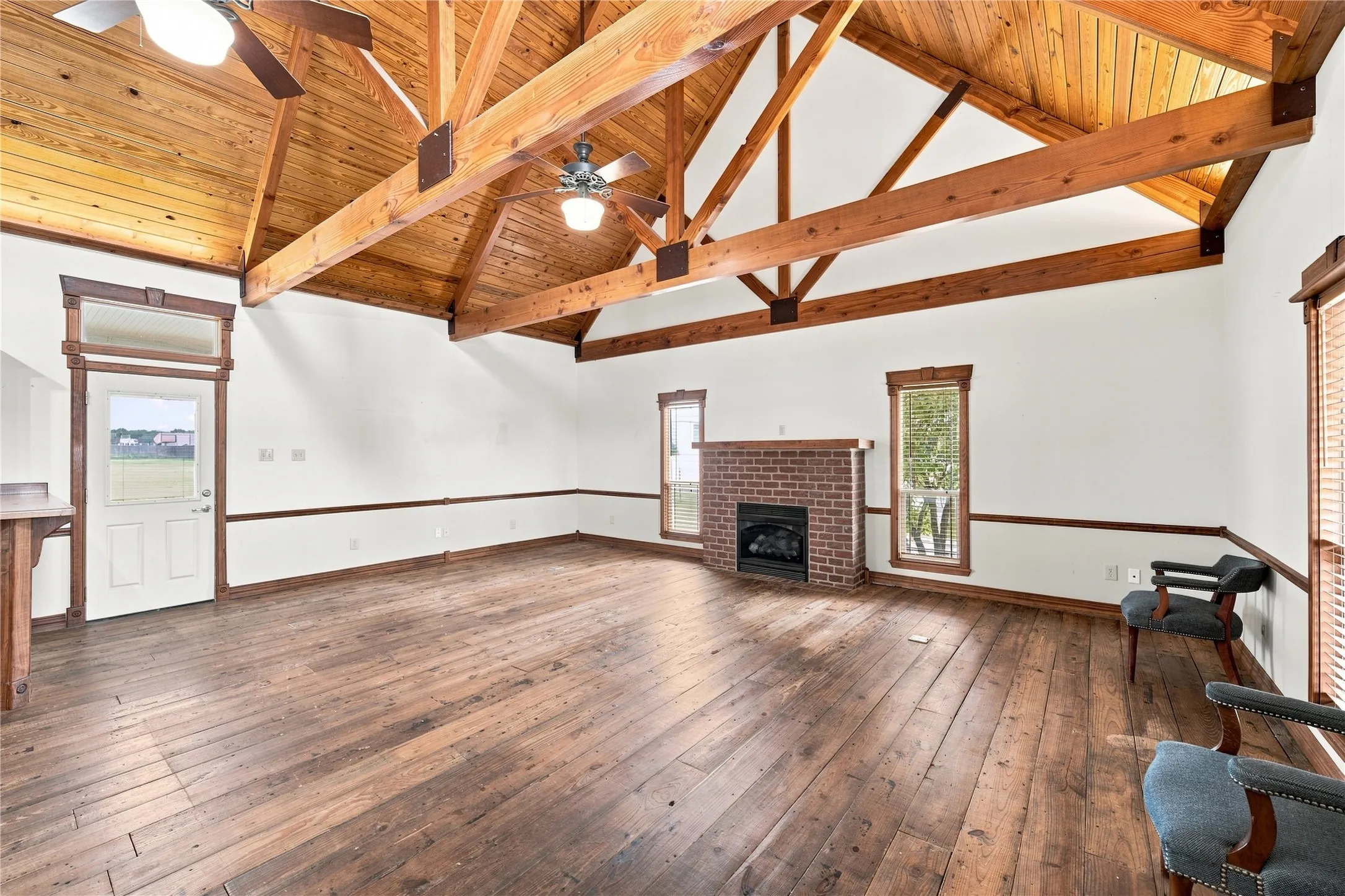 Vaulted wood-paneled ceiling with exposed beams, rich wood-finish flooring, brick fireplace with a wood mantle, and ceiling fans