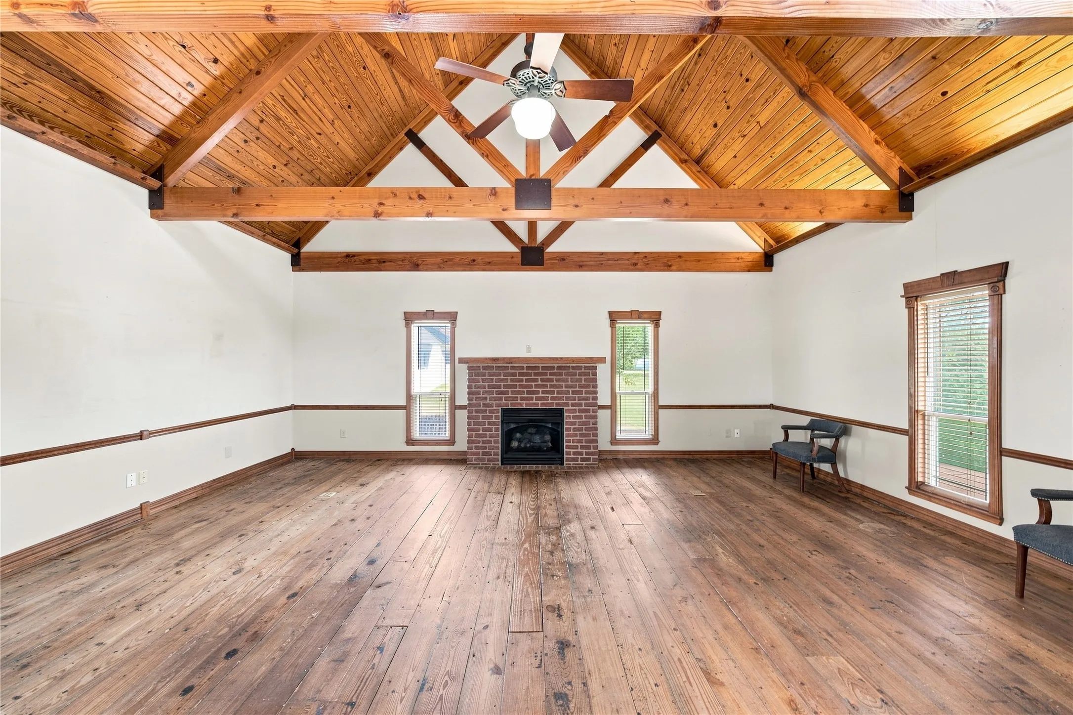 Vaulted wood-paneled ceiling with exposed beams, brick fireplace, wood-finish flooring, and multiple windows