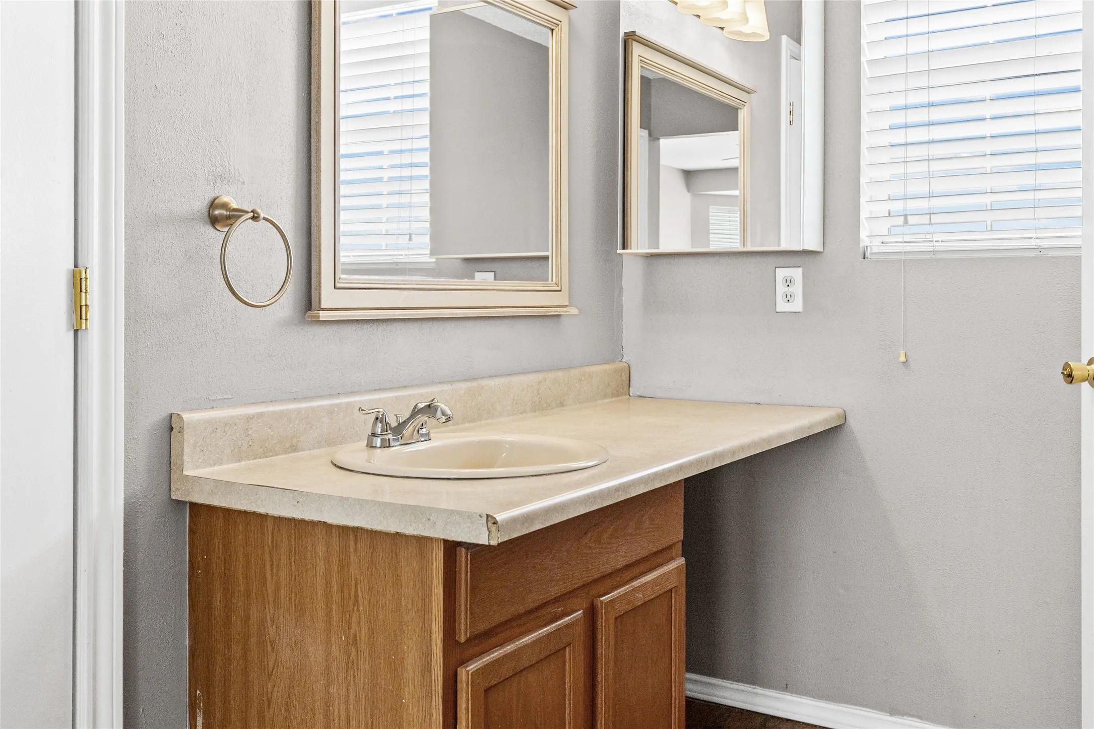 Cabinetry with wood-finish doors, integrated countertop with a drop-in sink, chrome-finish faucet, and framed wall mirror