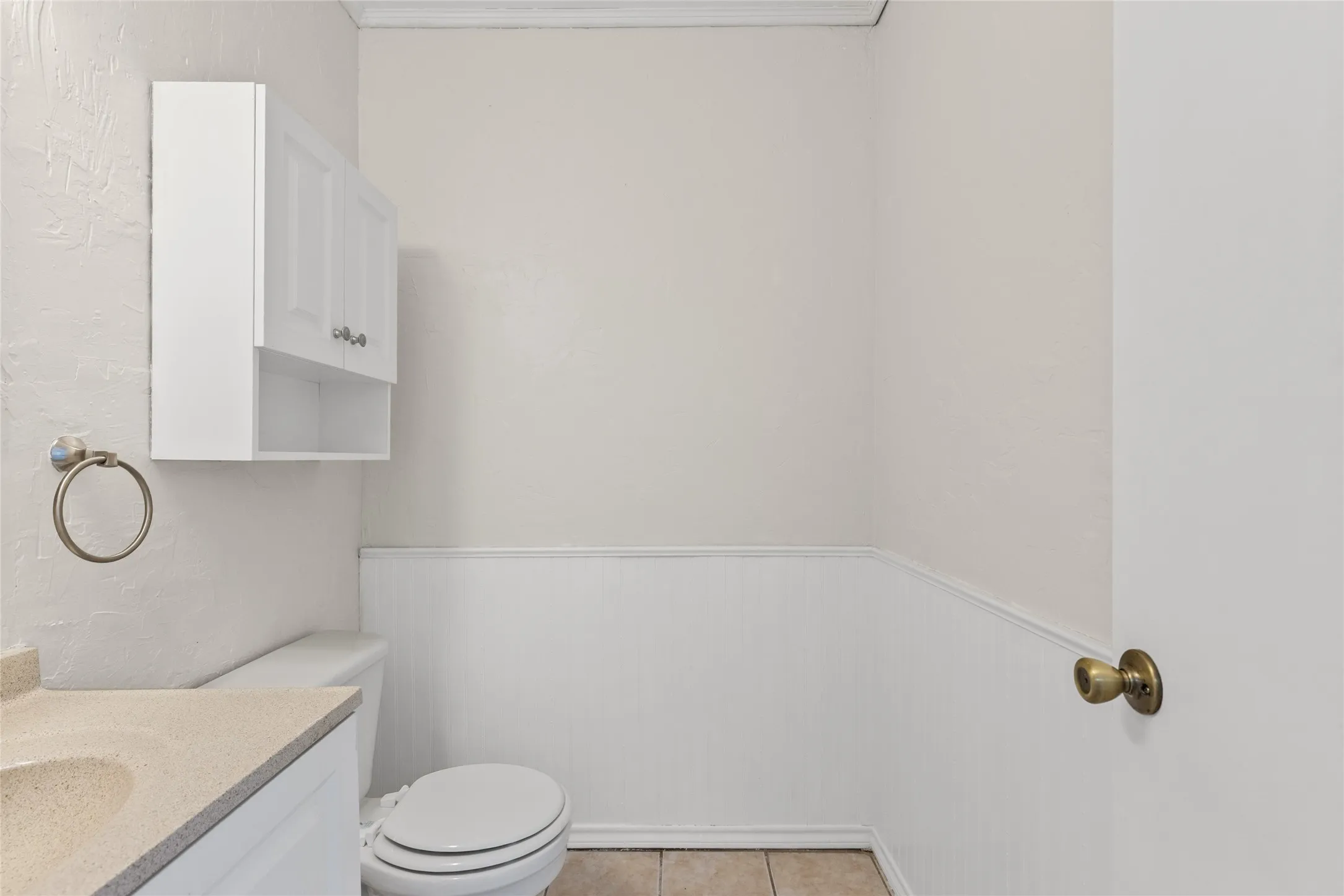 White wall-mounted cabinetry, integrated sink with a light-toned countertop, and white wainscoting