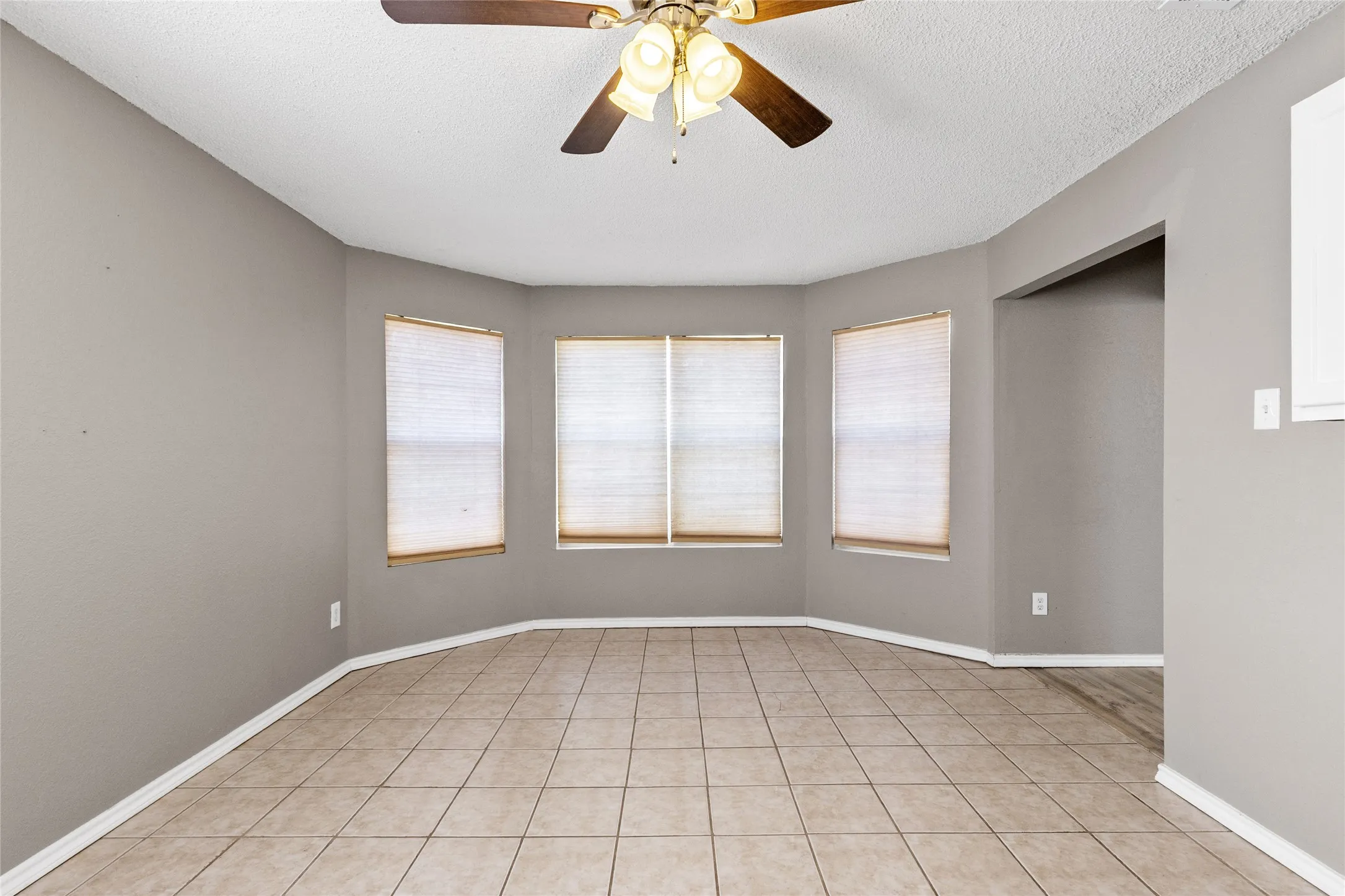 Tiled flooring, bay window with multiple windows, ceiling fan with integrated lighting, neutral wall tones, and crown molding