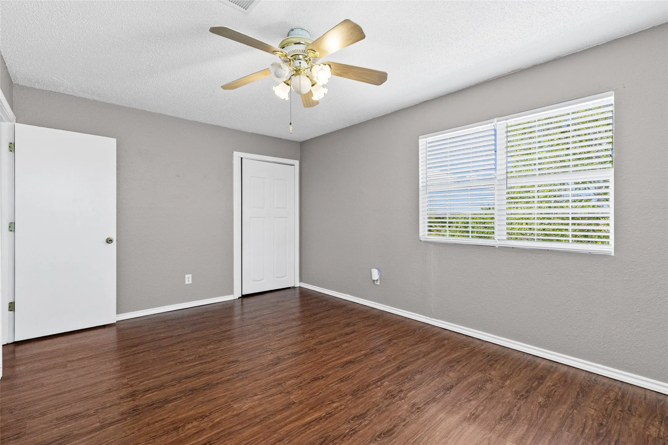 Wood-finish flooring, neutral gray wall tones, ceiling fan with light fixture, and white window blinds