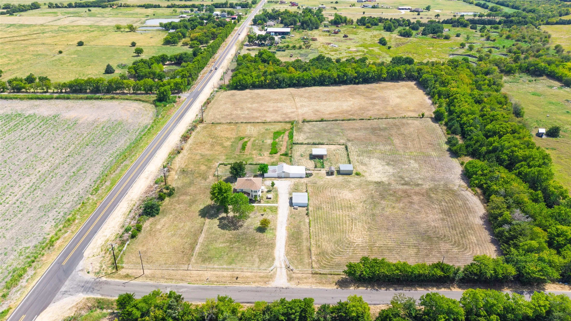 Expansive rural property featuring multiple outbuildings, established trees, and surrounding agricultural land