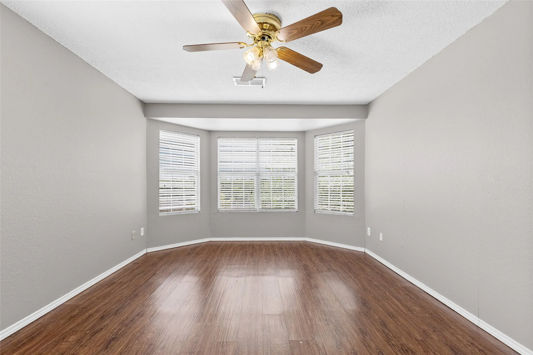 Bay window featuring three large windows with blinds, wood-finish flooring, and a ceiling fan with integrated lighting
