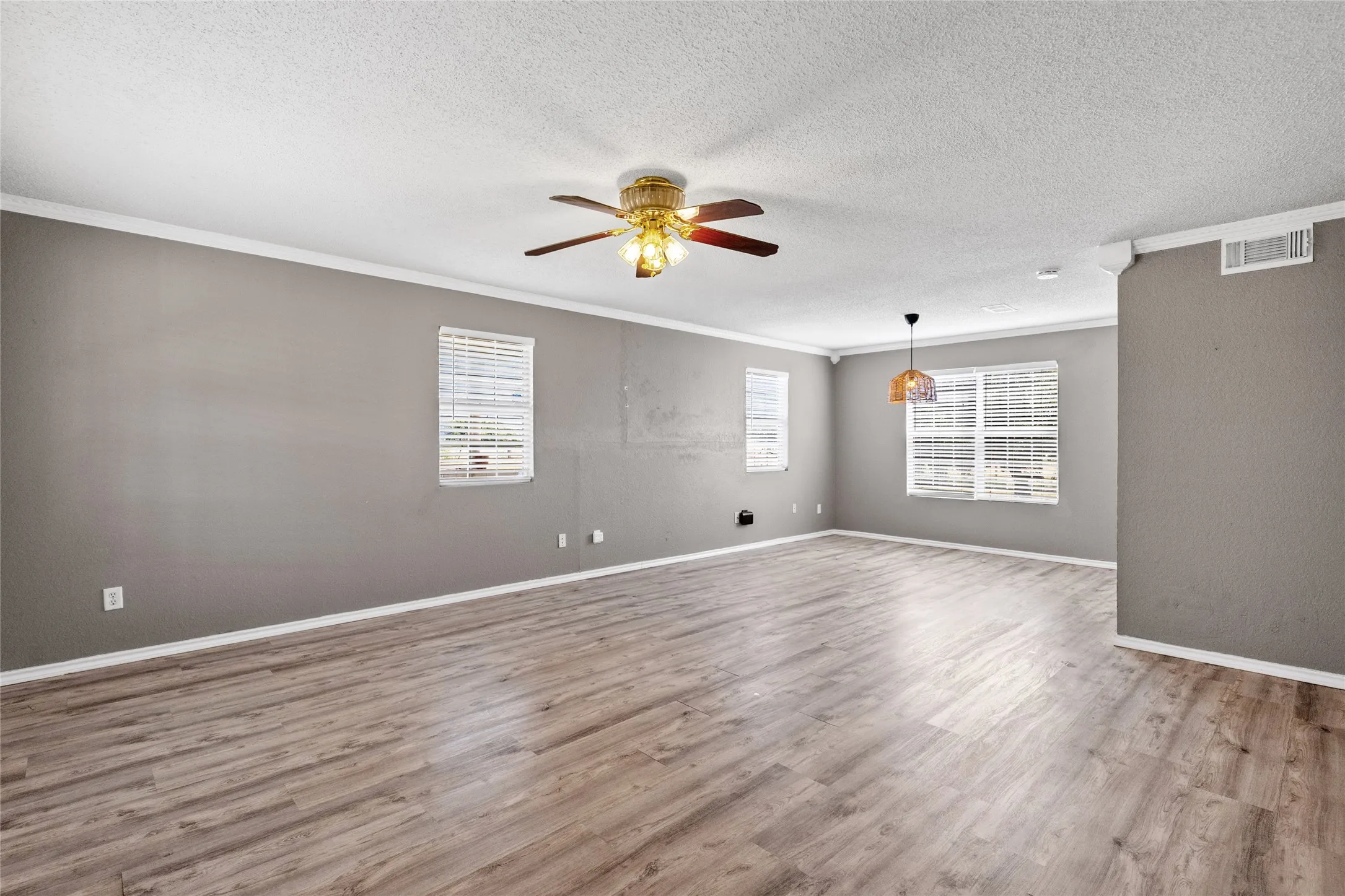 Spacious interior featuring wood-finish flooring, neutral paint, crown molding, and a ceiling fan with integrated lighting