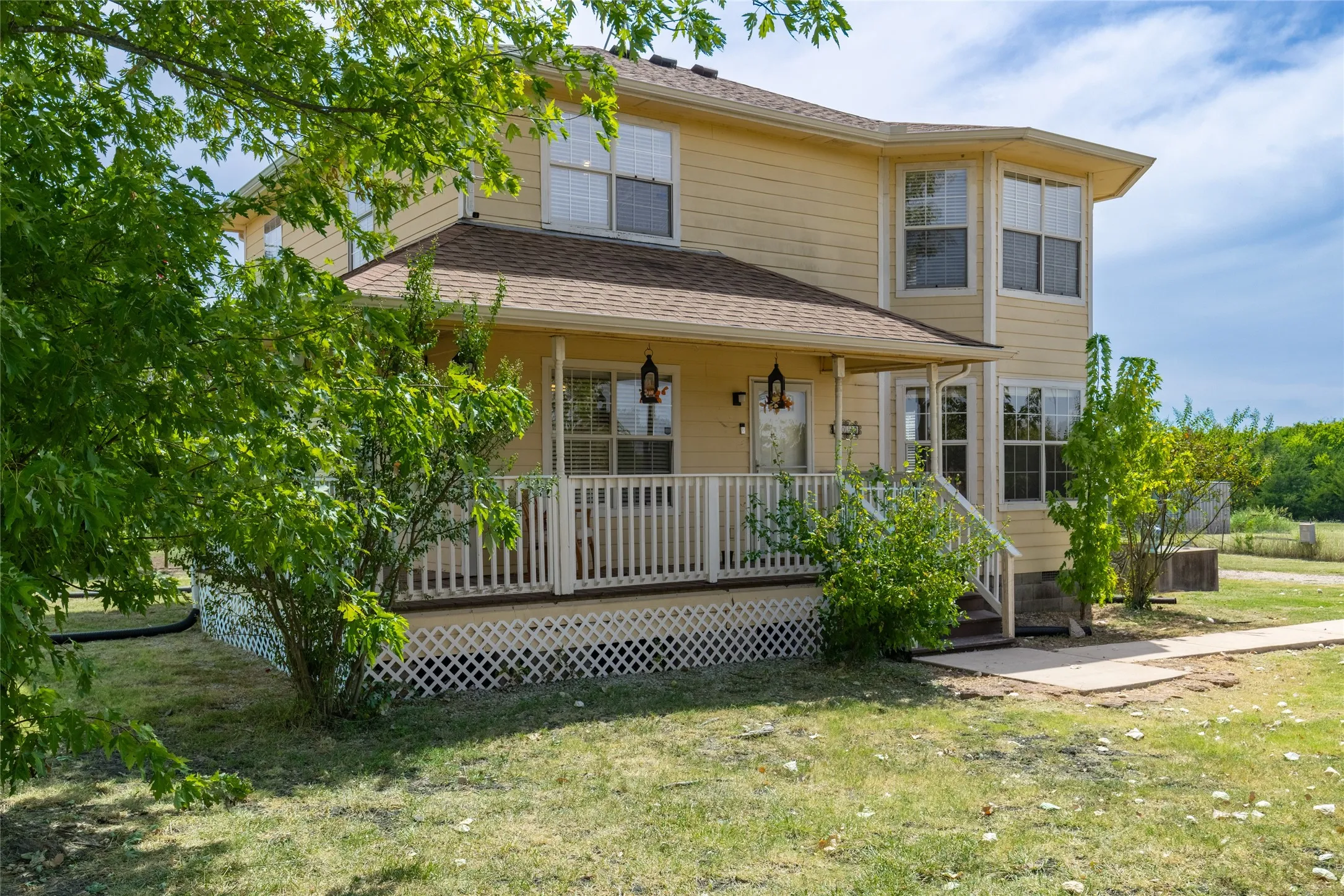 Two-story residence featuring a covered front porch, white railing, decorative lattice skirting, and a bay window