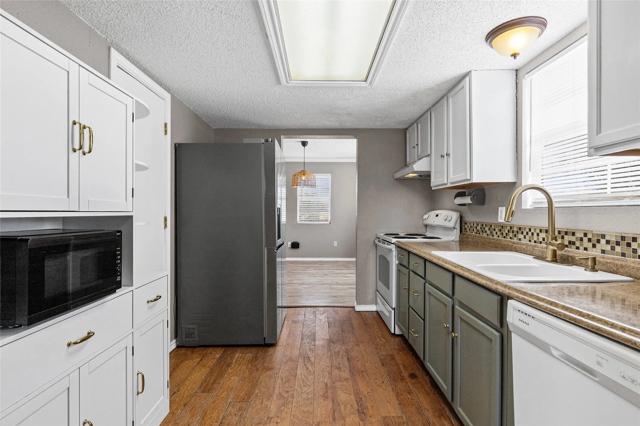 Kitchen featuring wood-finish flooring, two-tone cabinetry, mosaic tile backsplash, and a modern refrigerator