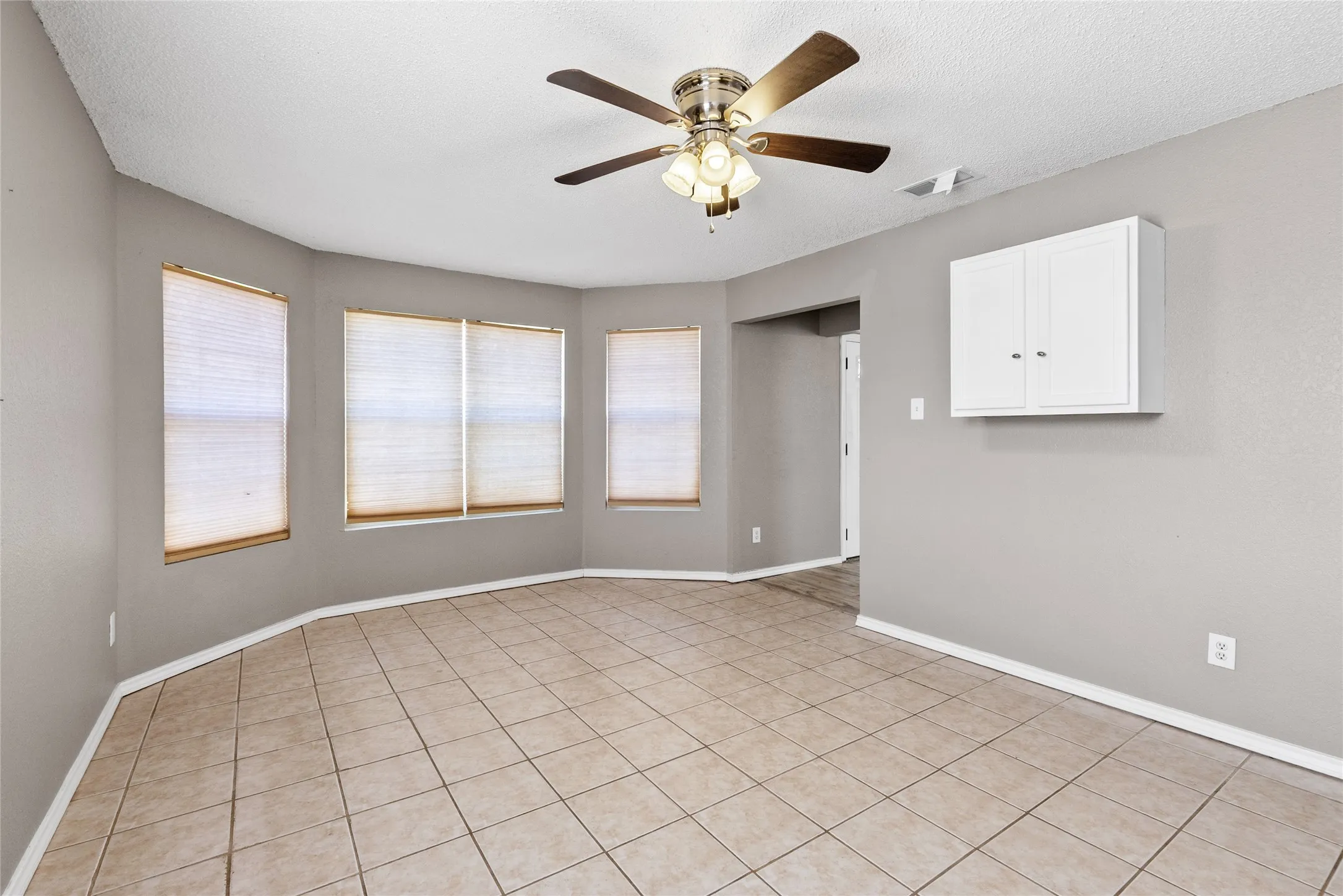 Tiled flooring, multiple windows, ceiling fan with light fixture, and wall-mounted cabinetry