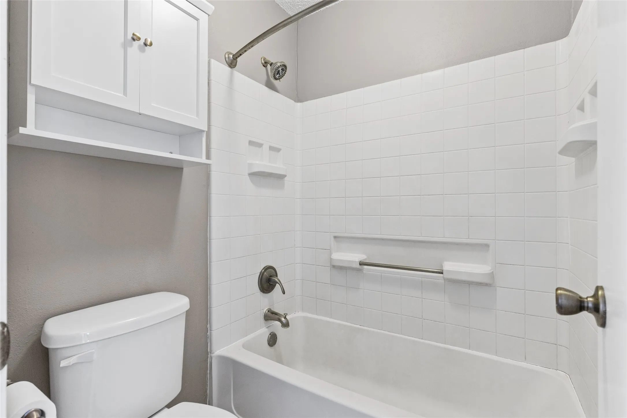 Clean, updated bathroom featuring white subway tile walls, a chrome showerhead and fixtures, a white porcelain toilet, and a soaking tub with integrated surround