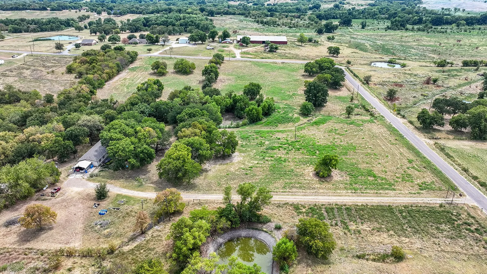 Expansive rural property featuring mature tree-lined grounds, established pastureland, and multiple outbuildings visible across the acreage