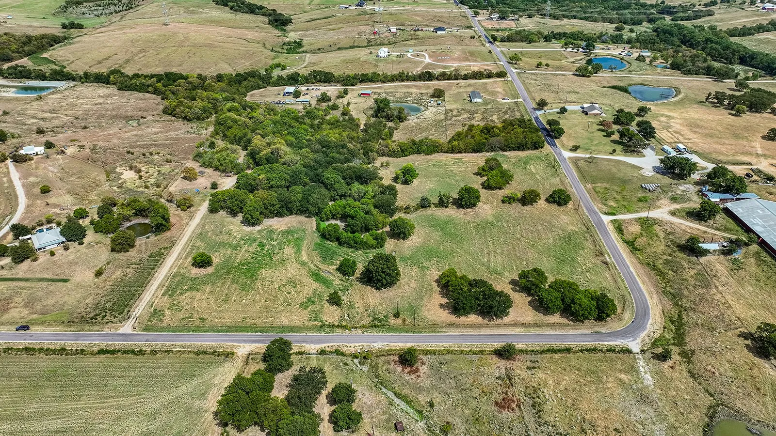 Expansive land parcel featuring open fields, a wooded area, and road frontage
