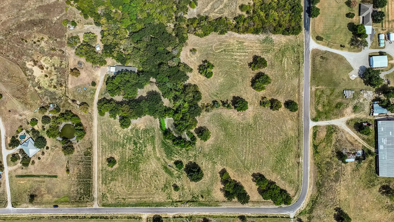 Expansive land parcel with open fields and wooded areas, featuring two distinct road frontages