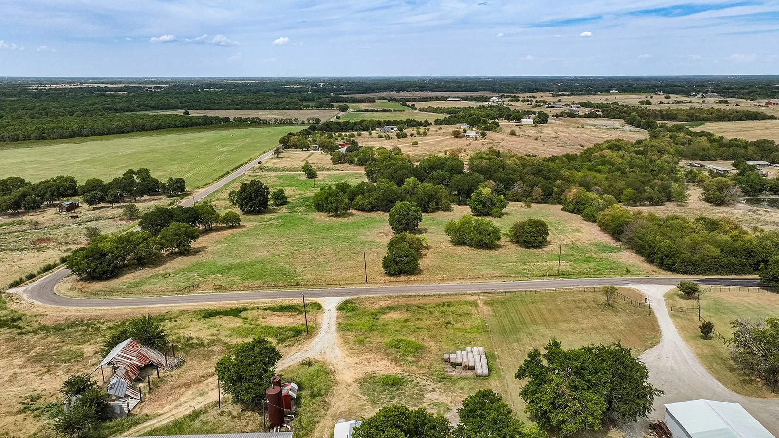 Expansive rural landscape featuring a paved road, scattered mature trees, and varied terrain with open fields