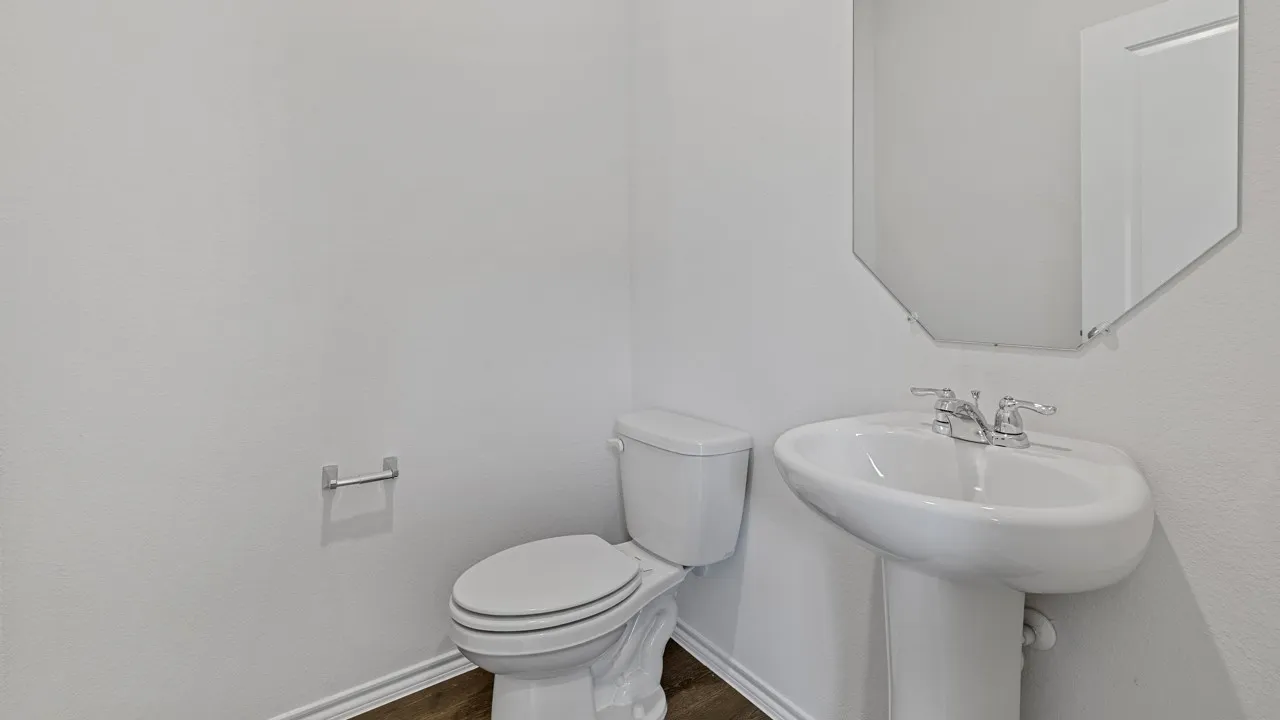 Pedestal sink with chrome fixtures, octagonal mirror, toilet, and wood-finish flooring
