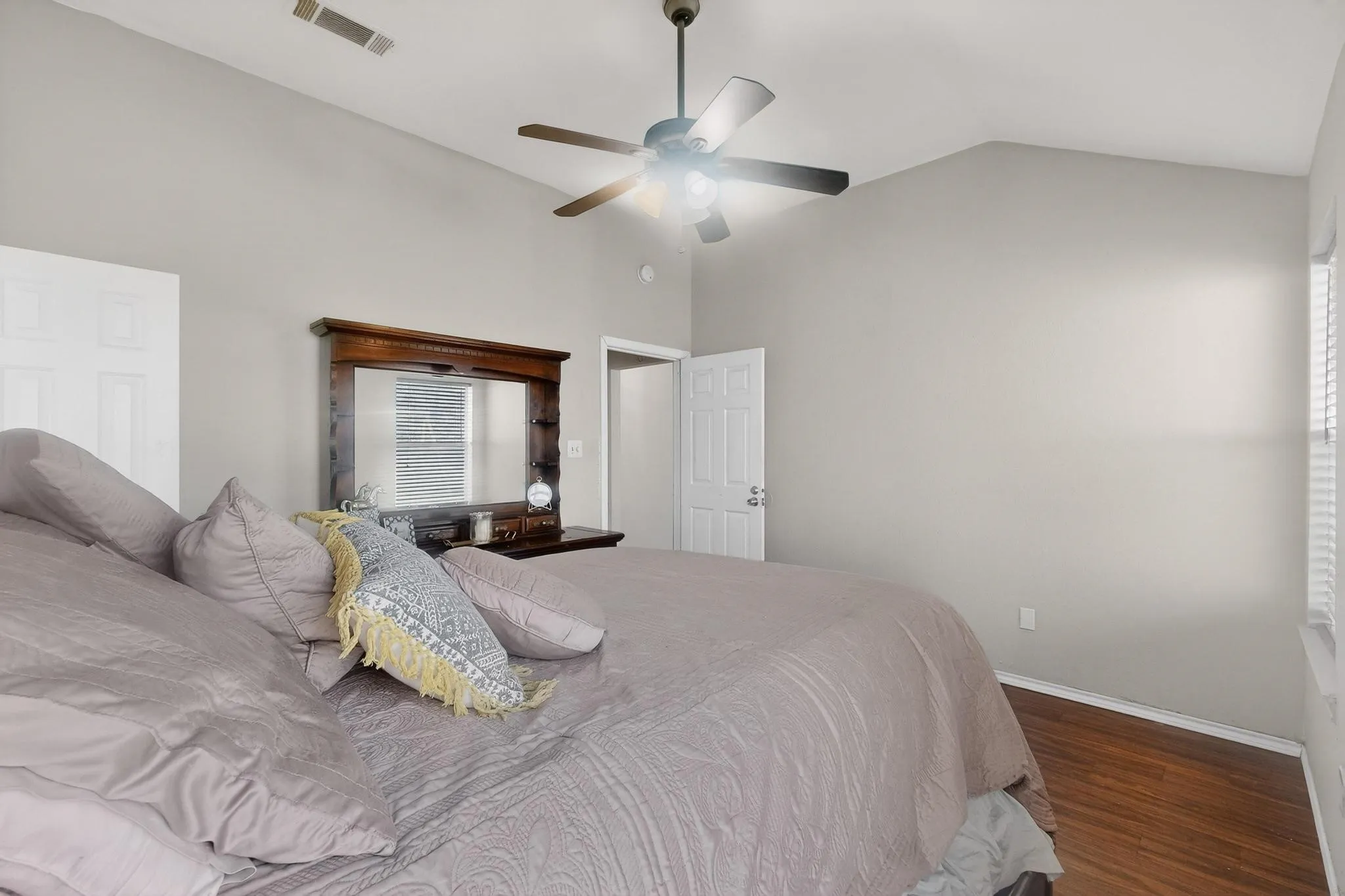 Vaulted ceiling with a ceiling fan, light gray wall paint, wood-finish flooring, and white window blinds