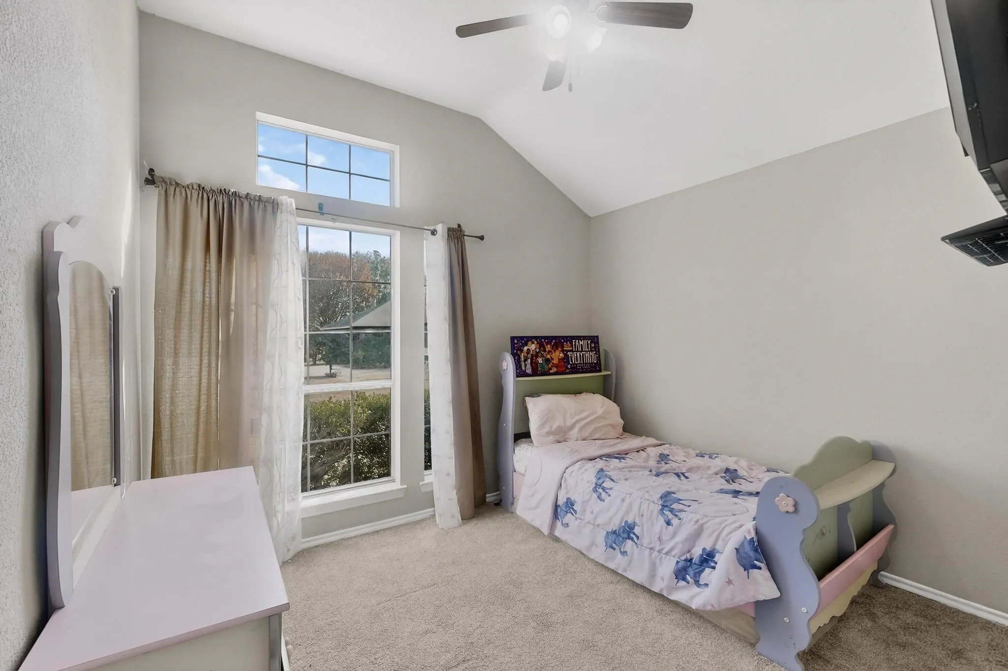 Vaulted ceiling, ceiling fan with light, large window with transom, and neutral carpet flooring