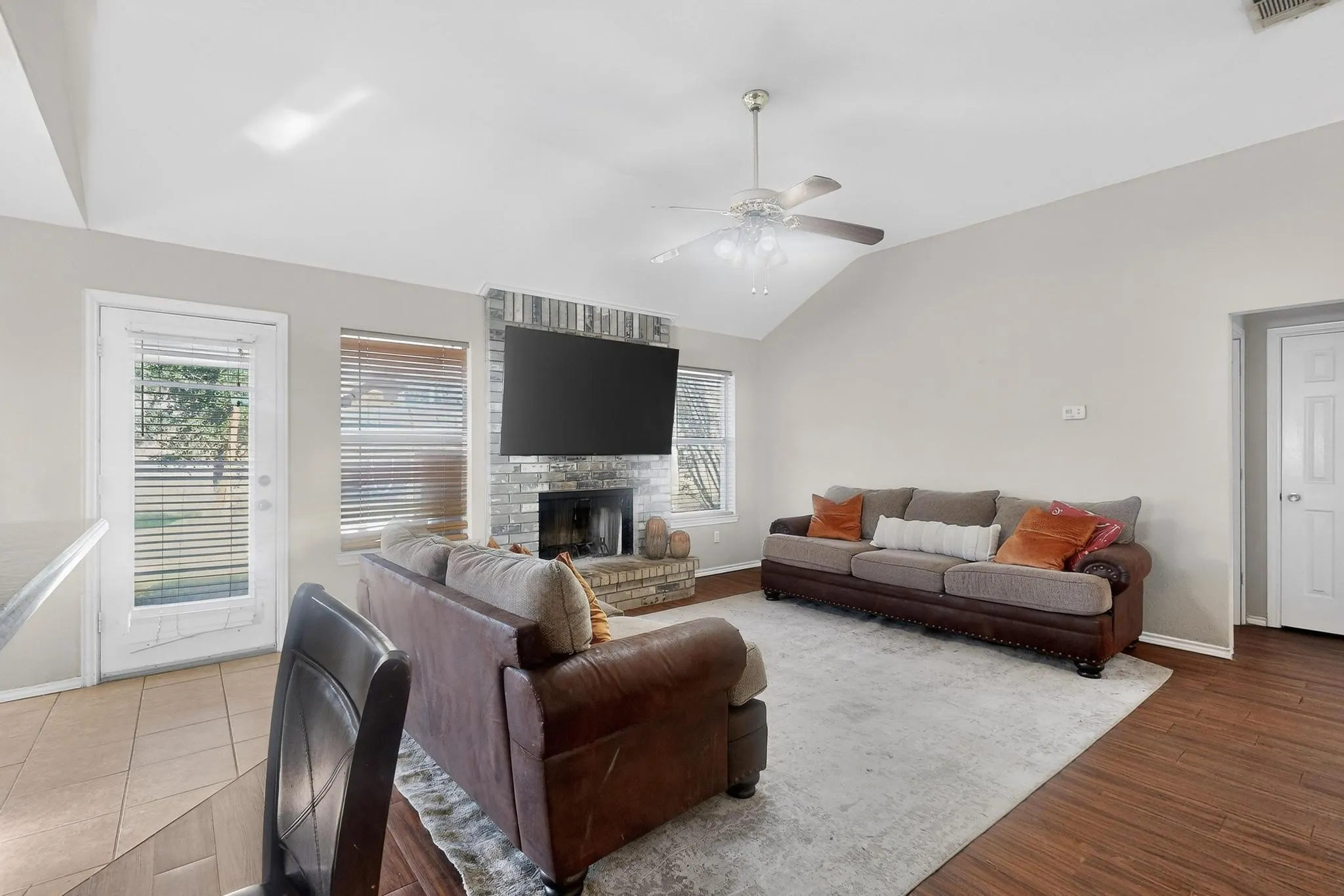 Vaulted ceiling with a ceiling fan, brick fireplace, wood-finish flooring, and a glass-paneled door