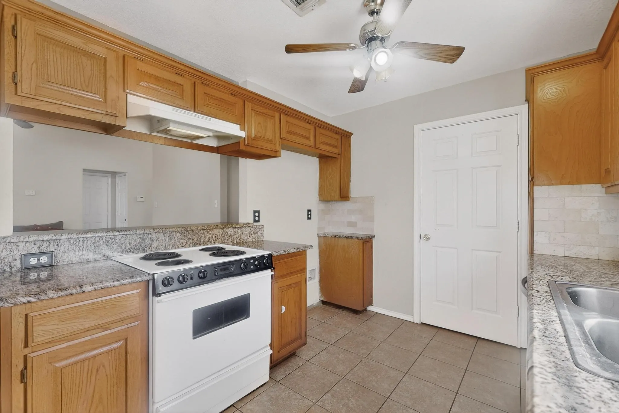 Kitchen featuring wood cabinetry, light-toned countertops, a white range, a stainless steel sink, and tile flooring