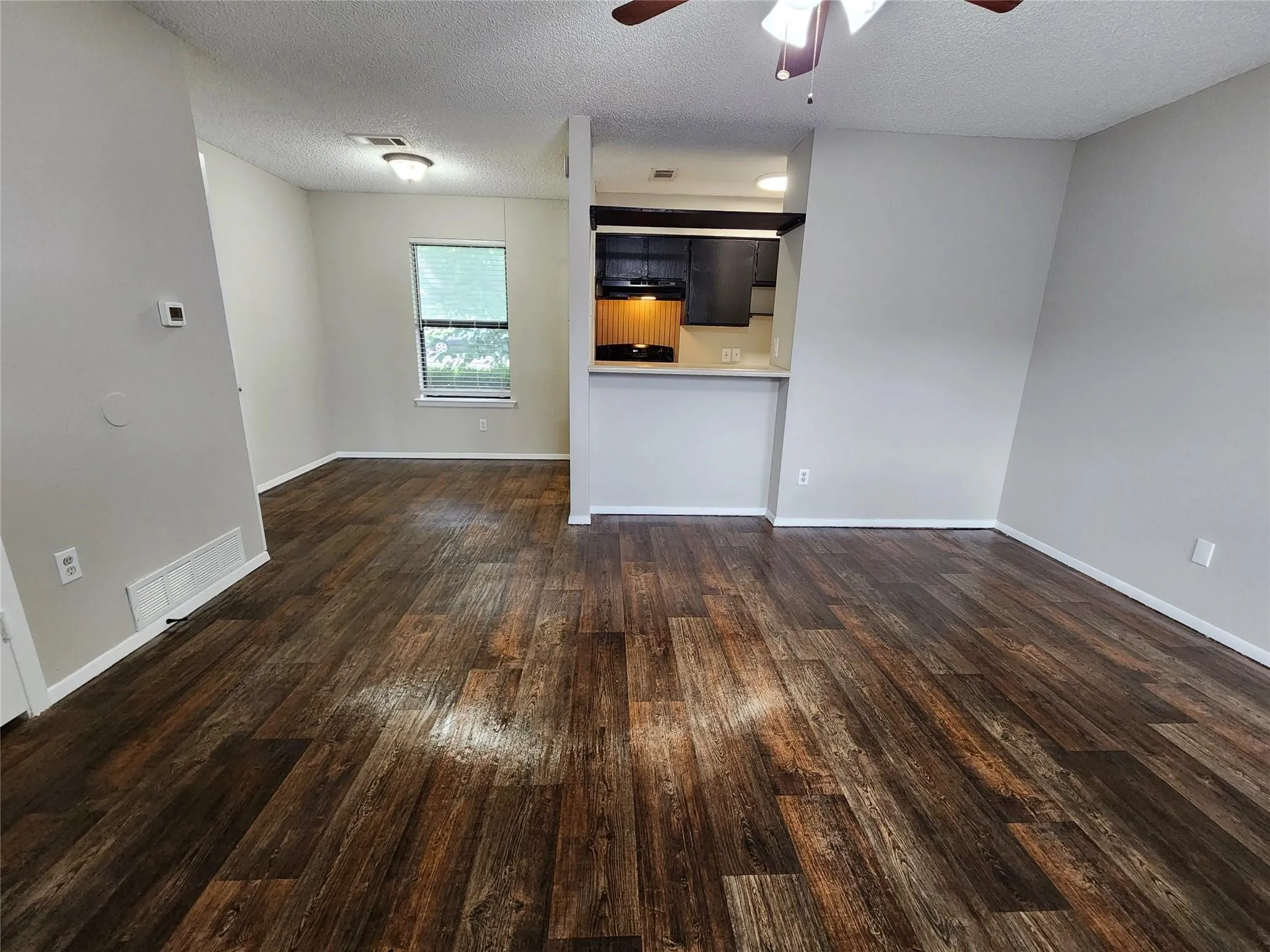 Wood-finish flooring throughout, ceiling fan with integrated lighting, and a kitchen pass-through with a breakfast bar