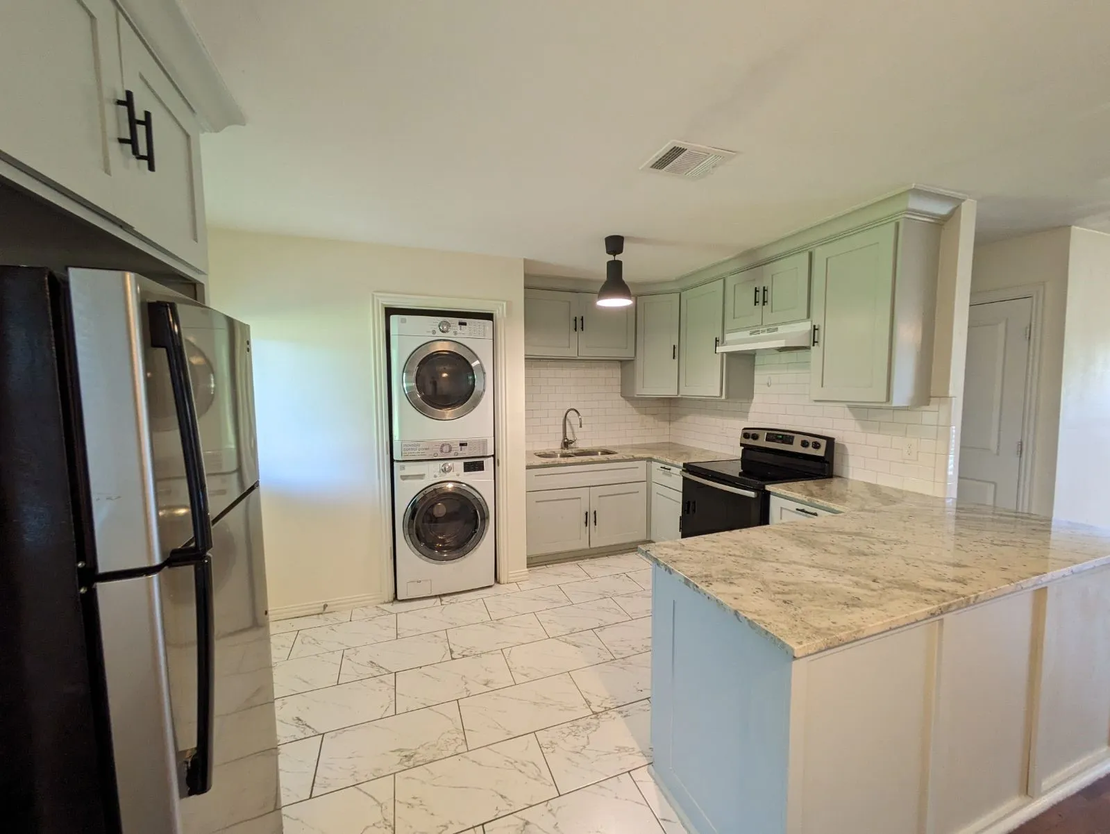 Kitchen featuring backsplash, appliances with stainless steel finishes, sink, light stone counters, and stacked washer and dryer
