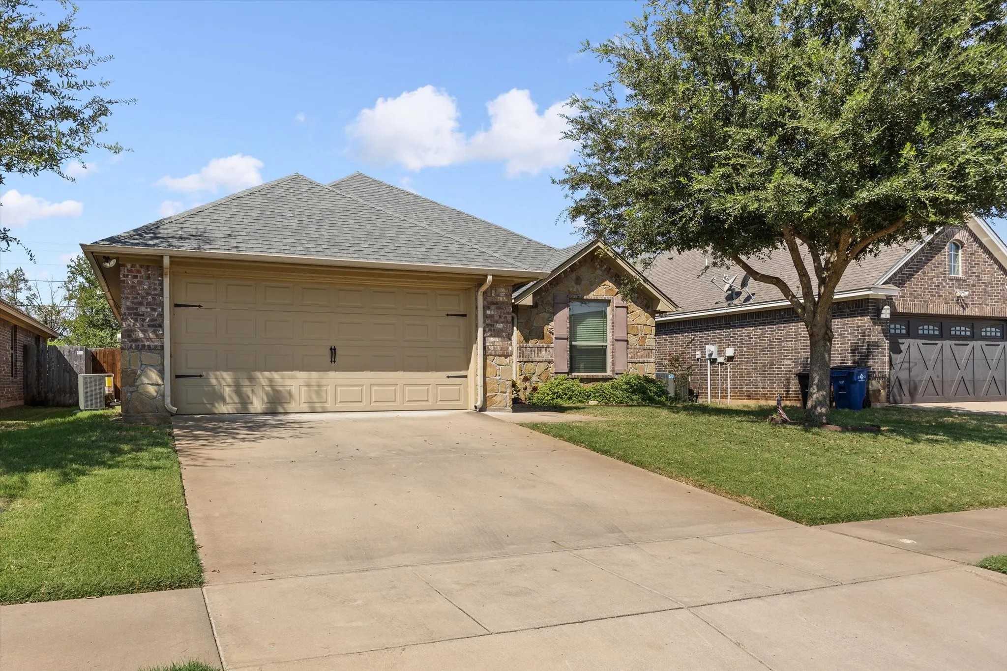 Brick and stone exterior with a neutral garage door, a concrete driveway, and mature landscaping