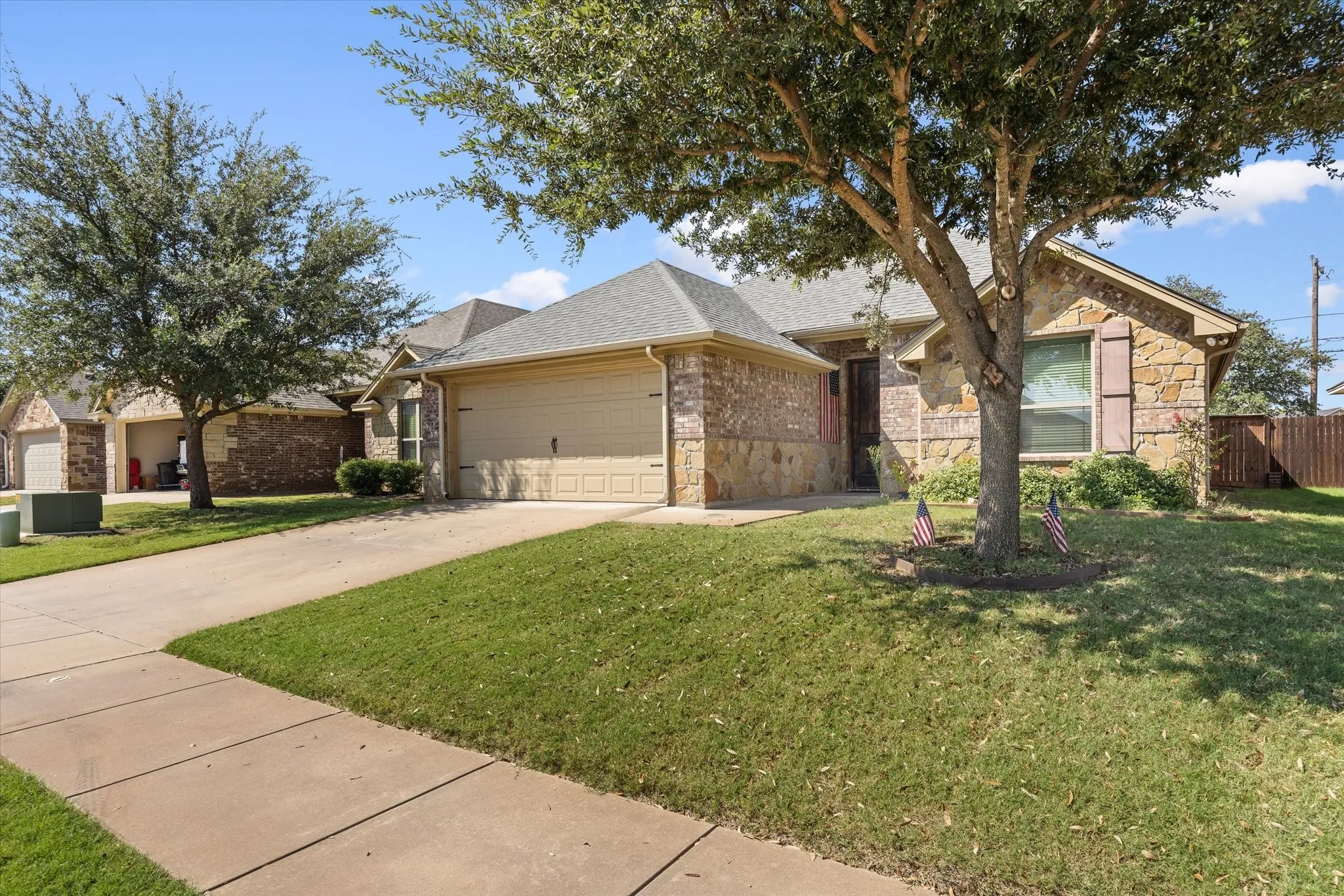 Stone and brick exterior with a tan garage door, a concrete driveway, and a sidewalk