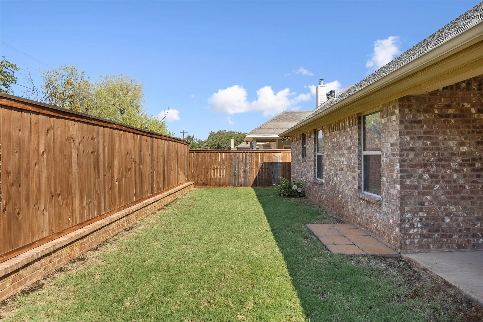 Private backyard featuring a manicured lawn, full privacy fencing, brick exterior, and a concrete patio