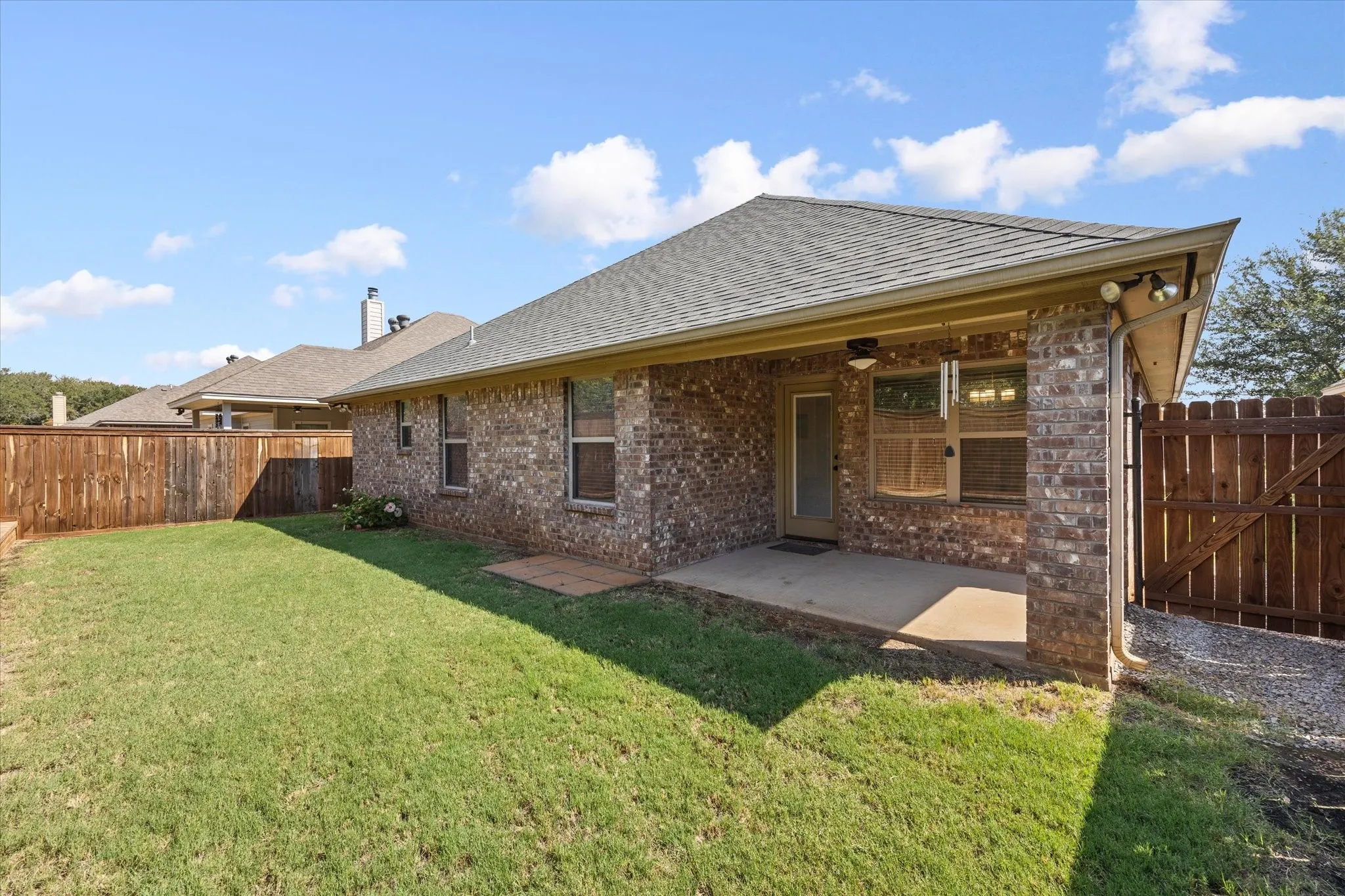 Back of structure featuring a manicured lawn, brick exterior, covered patio, and wood privacy fencing