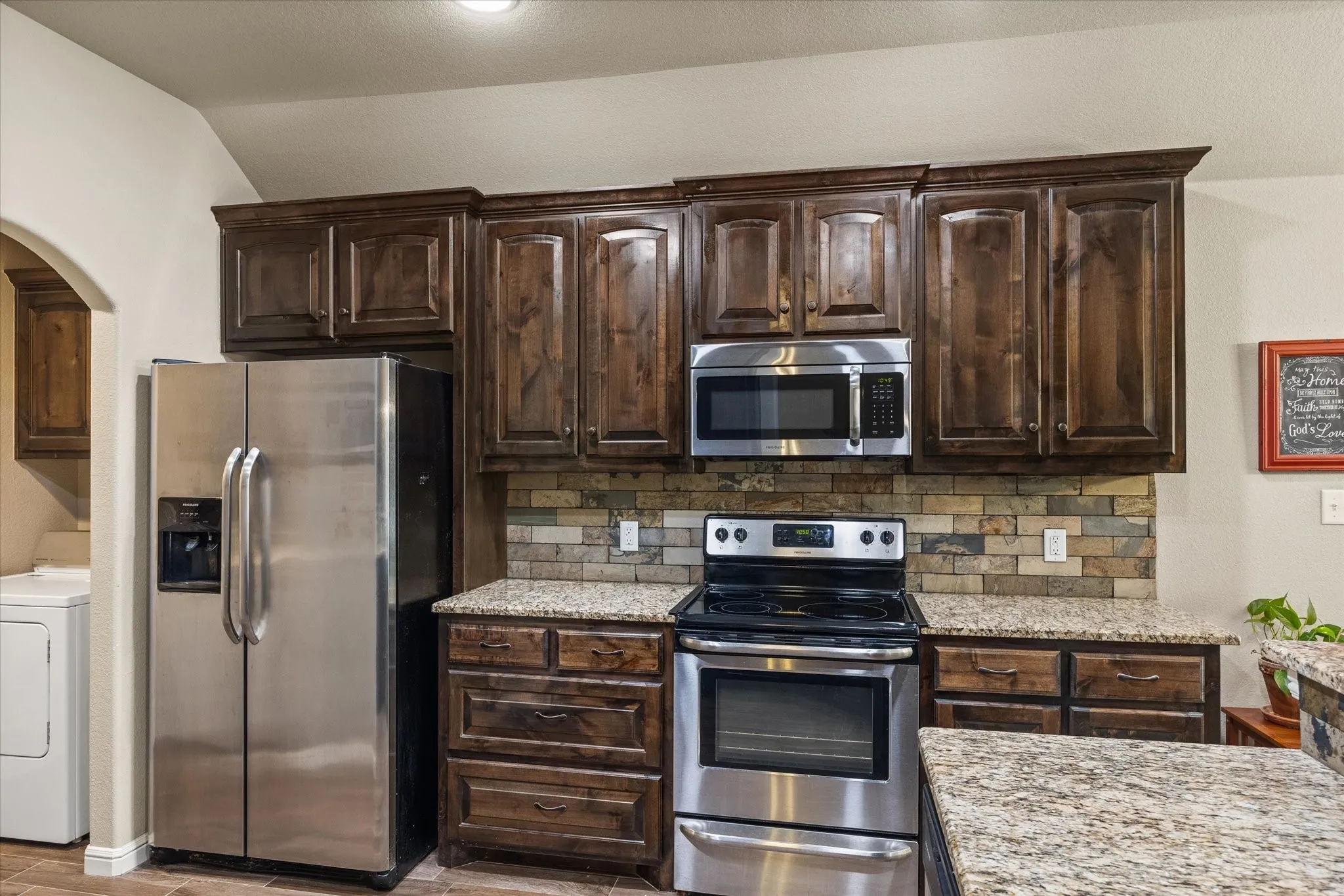 Dark wood-finish cabinetry, stainless steel appliances, tile backsplash, and granite countertops