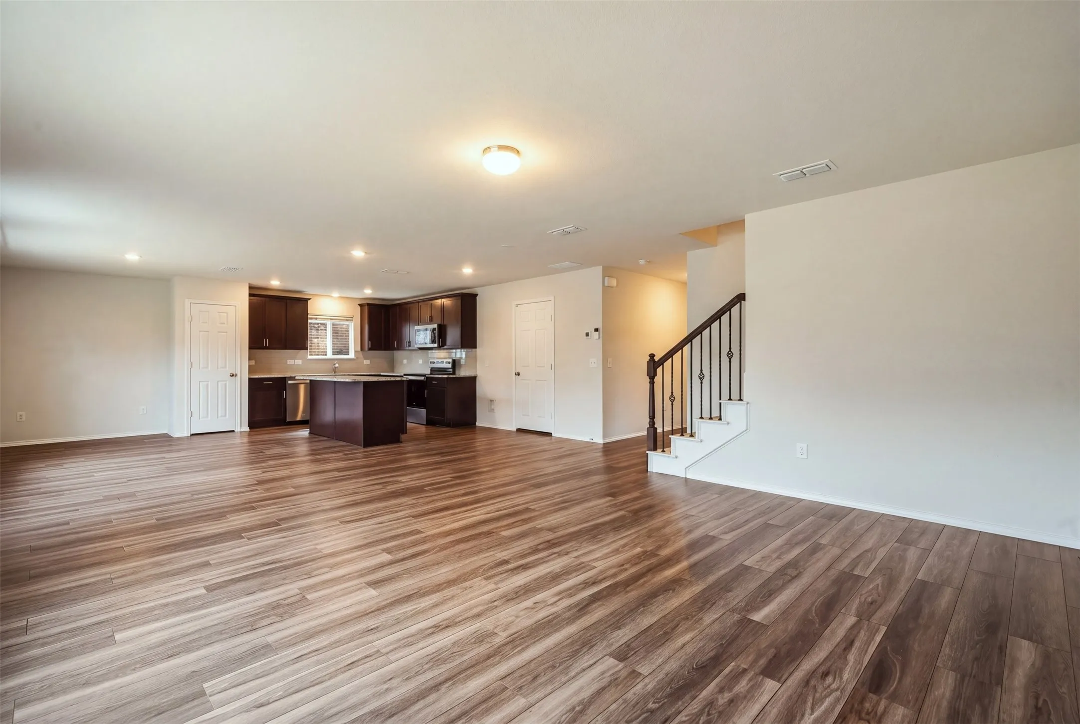 Bright open-concept living space with wood-look floors, recessed lighting, and a stylish kitchen with dark cabinetry, island, and stainless steel appliances