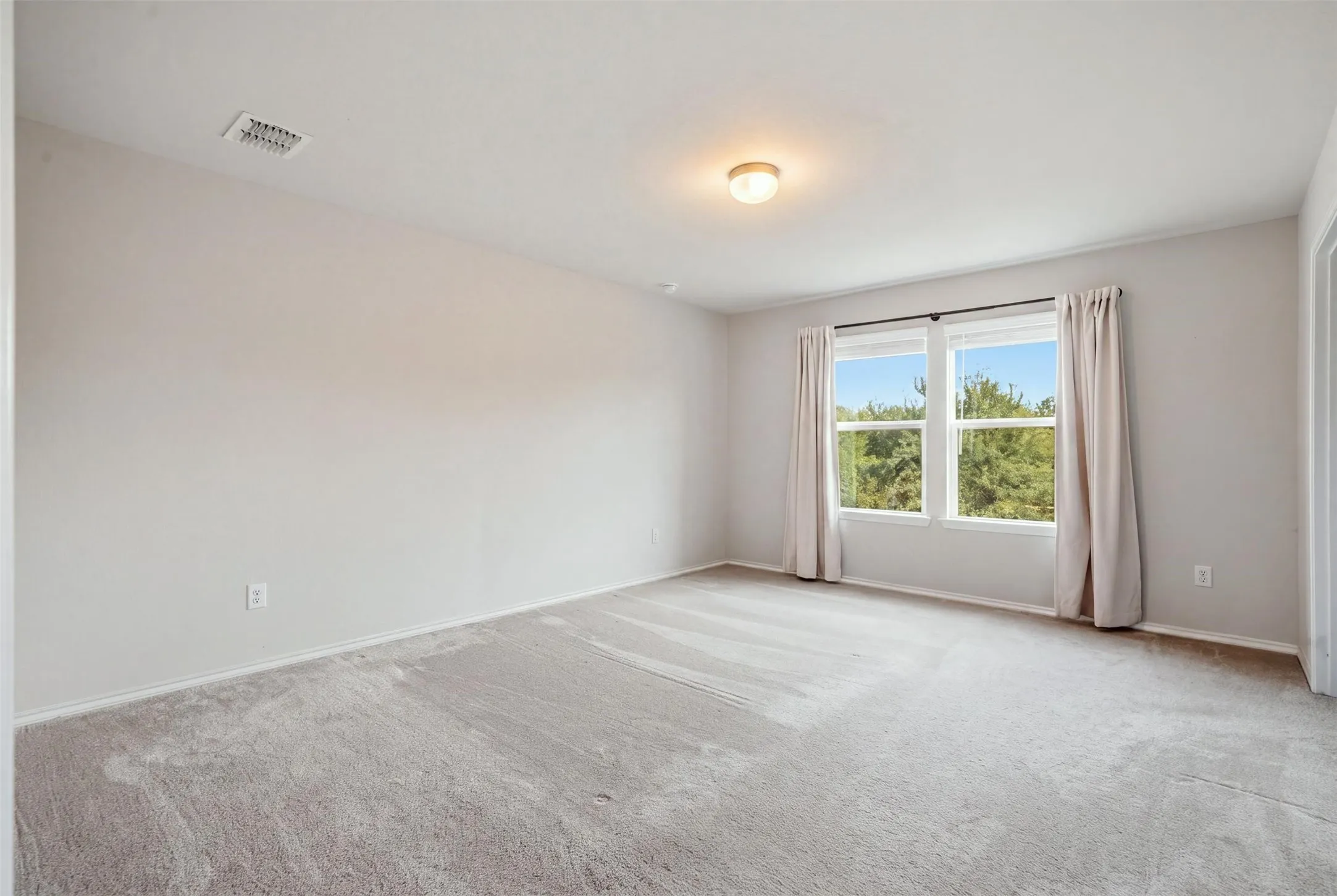 Bright, inviting space with light carpeting, large windows, white frames, recessed lighting, and neutral walls
