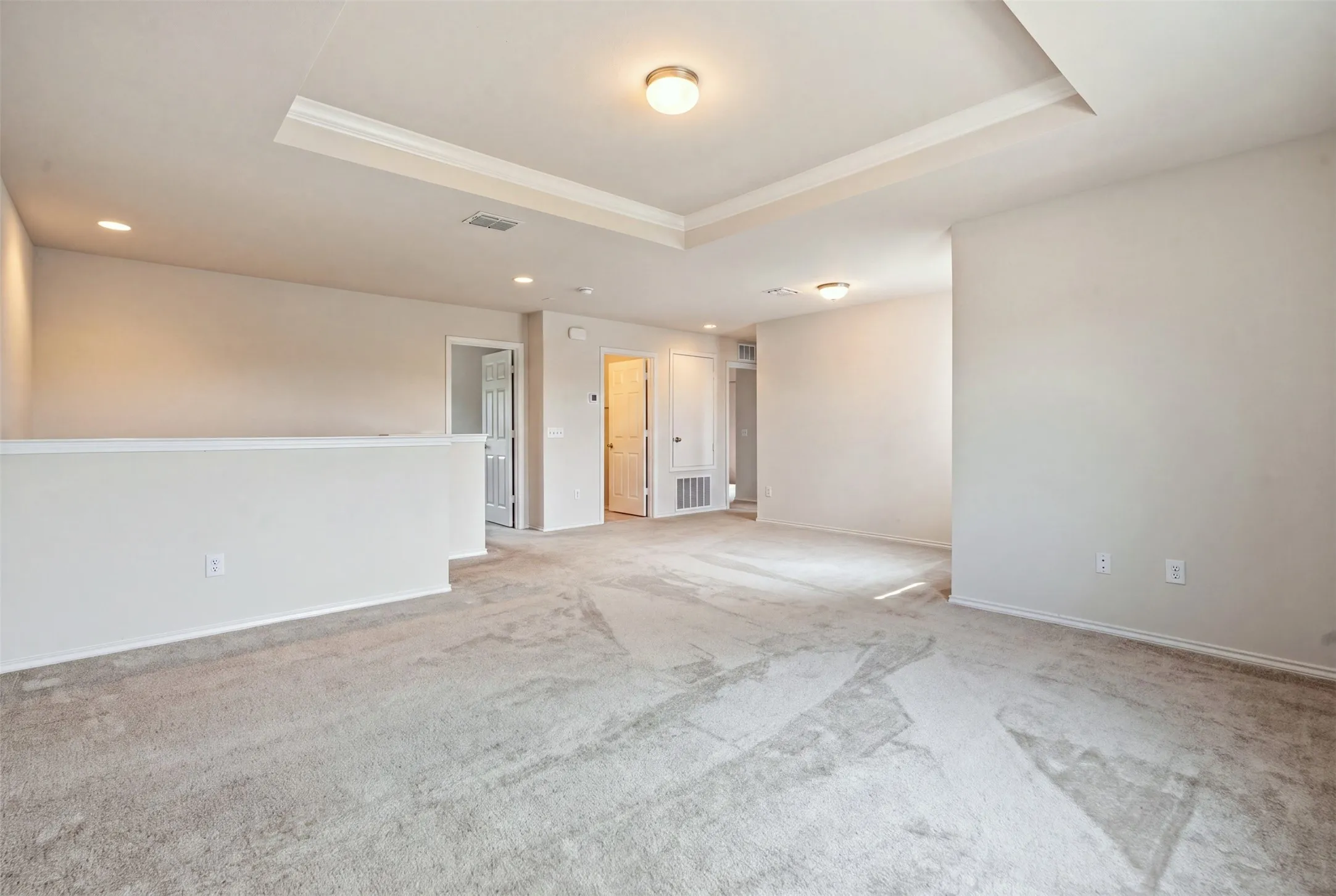 Spacious carpeted room with a tray ceiling, recessed lighting, and a soft neutral color palette
