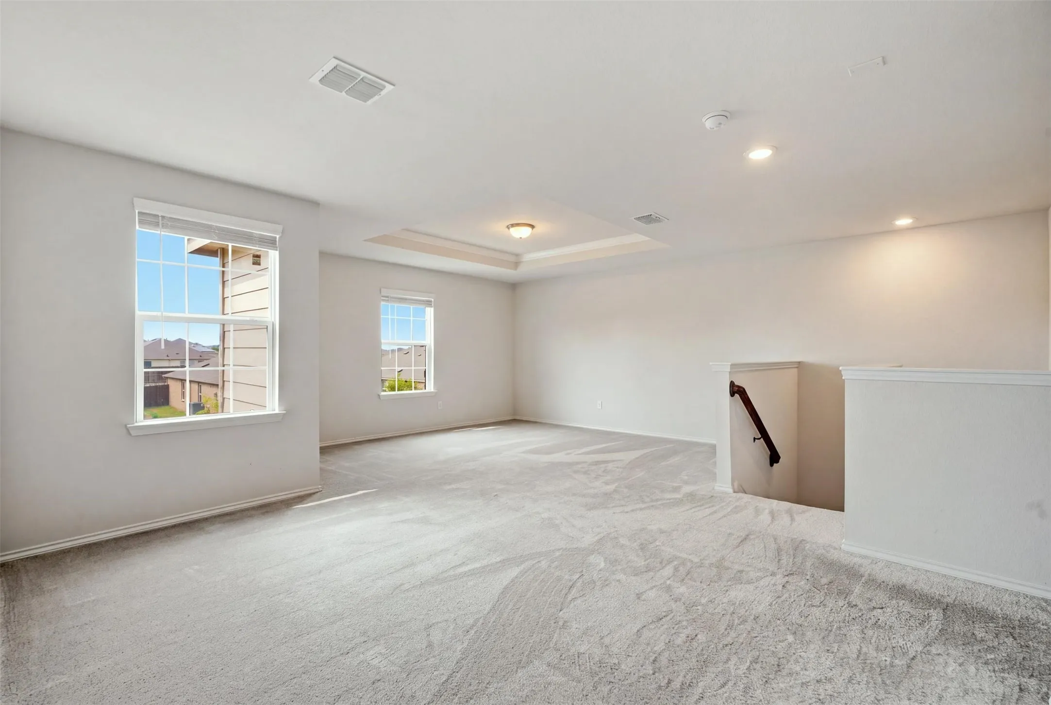 Spacious carpeted area with multiple windows, a tray ceiling, and recessed lighting for a bright, airy feel

