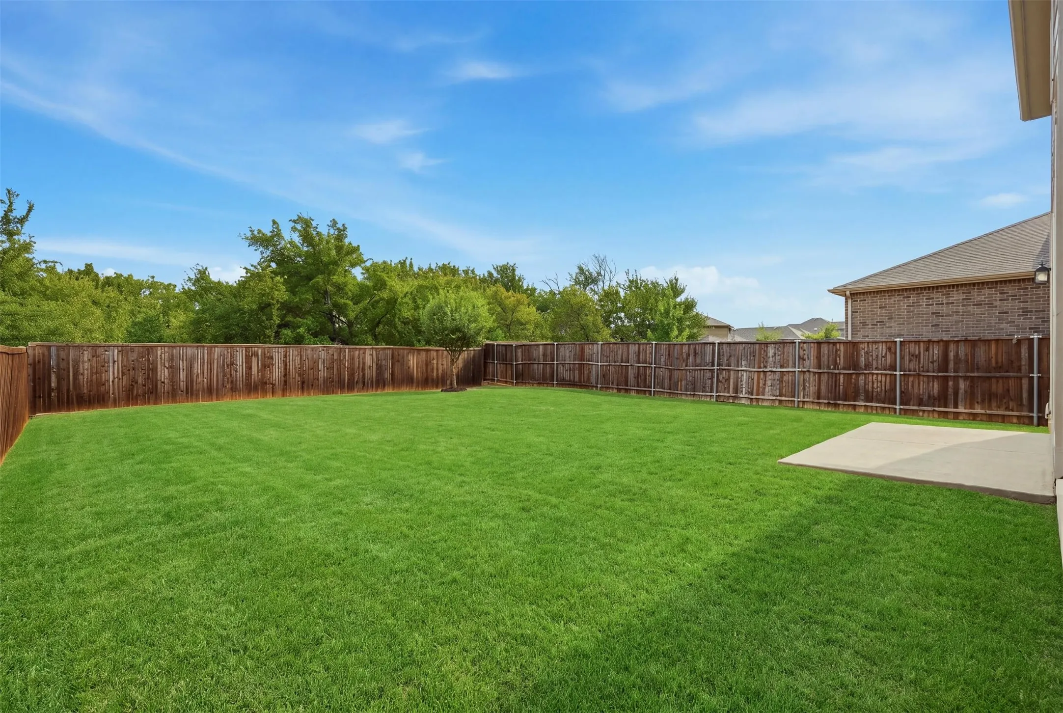 Expansive backyard with a manicured lawn, full privacy fencing, and a spacious concrete patio perfect for outdoor enjoyment
